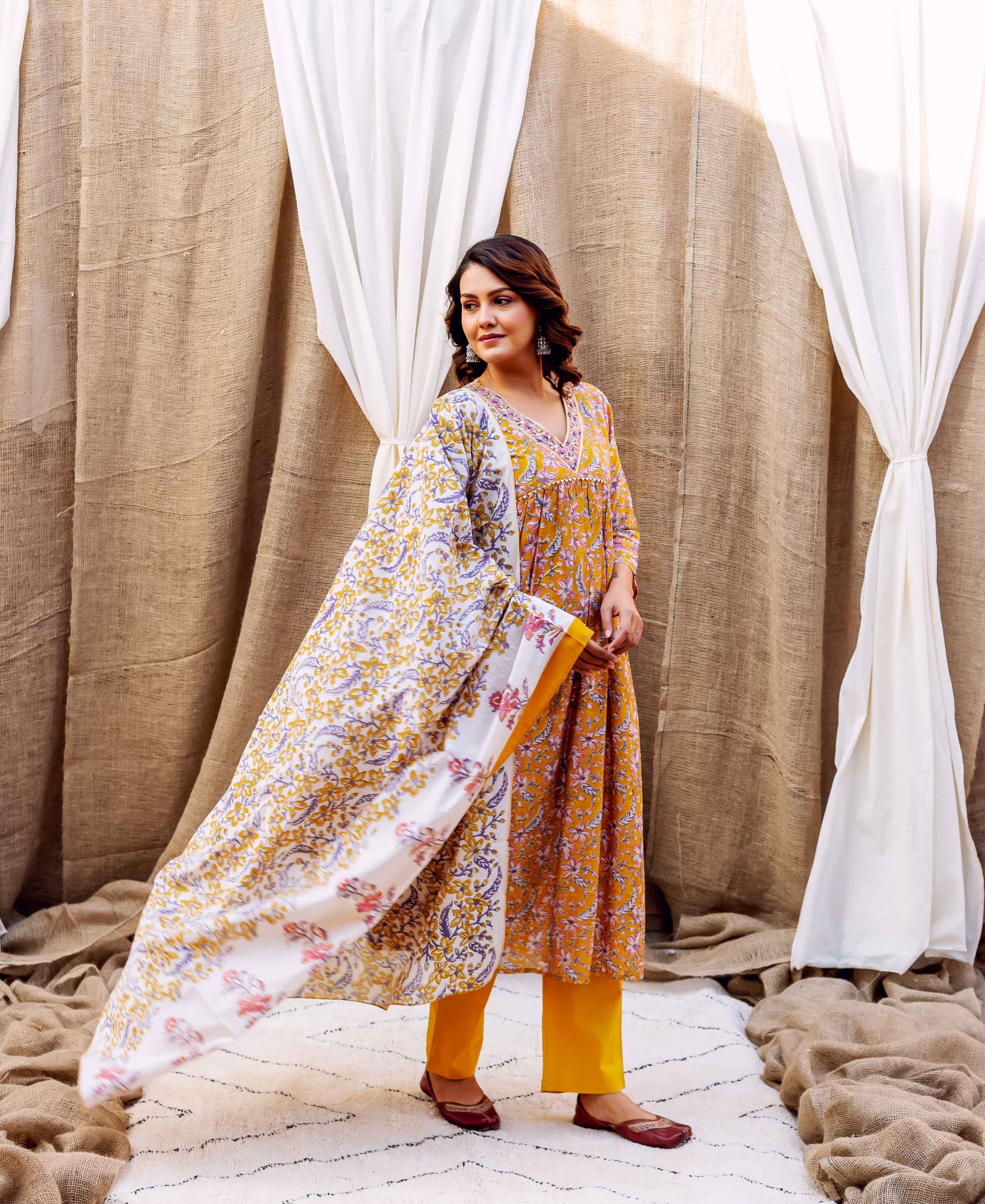 Woman in a golden spice block-printed kurta, pants, and flowing white floral dupatta.
