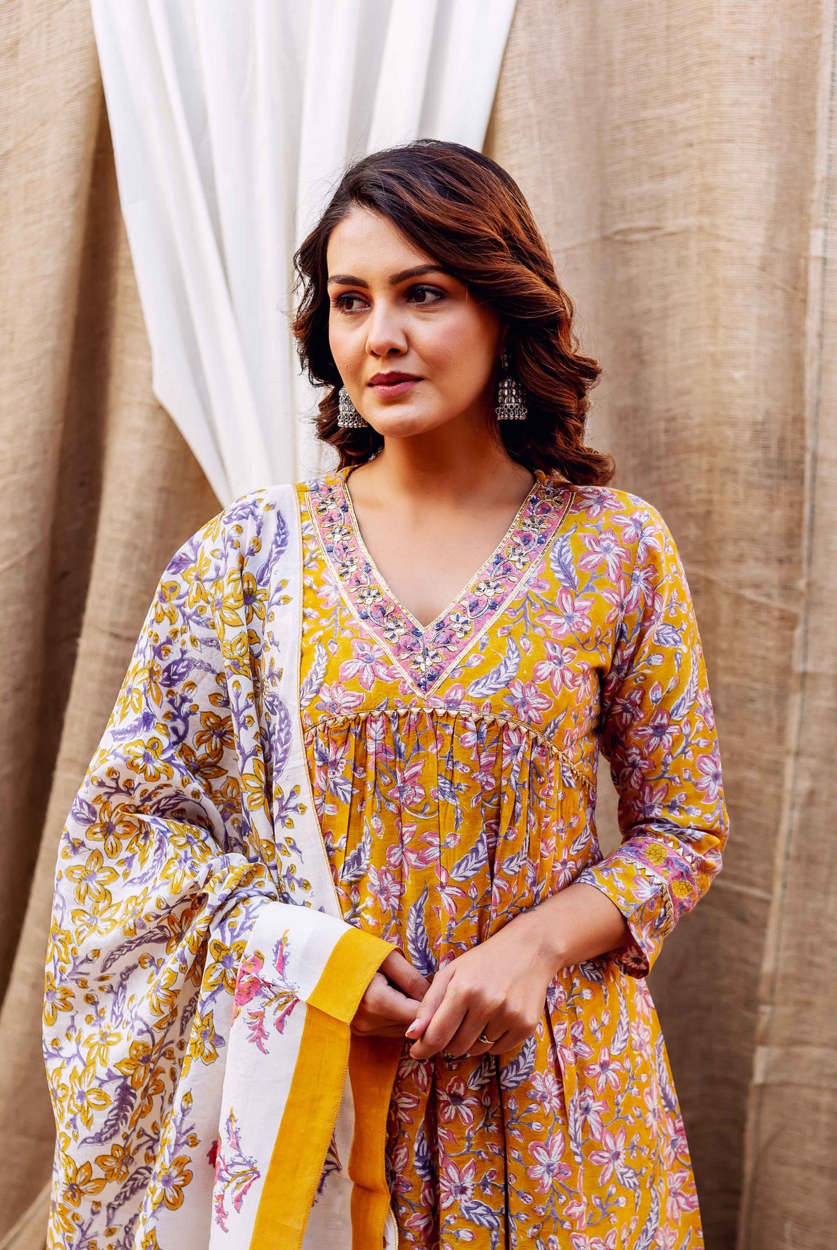 Model wears golden yellow block-printed kurta with pink and purple floral designs, matching dupatta.