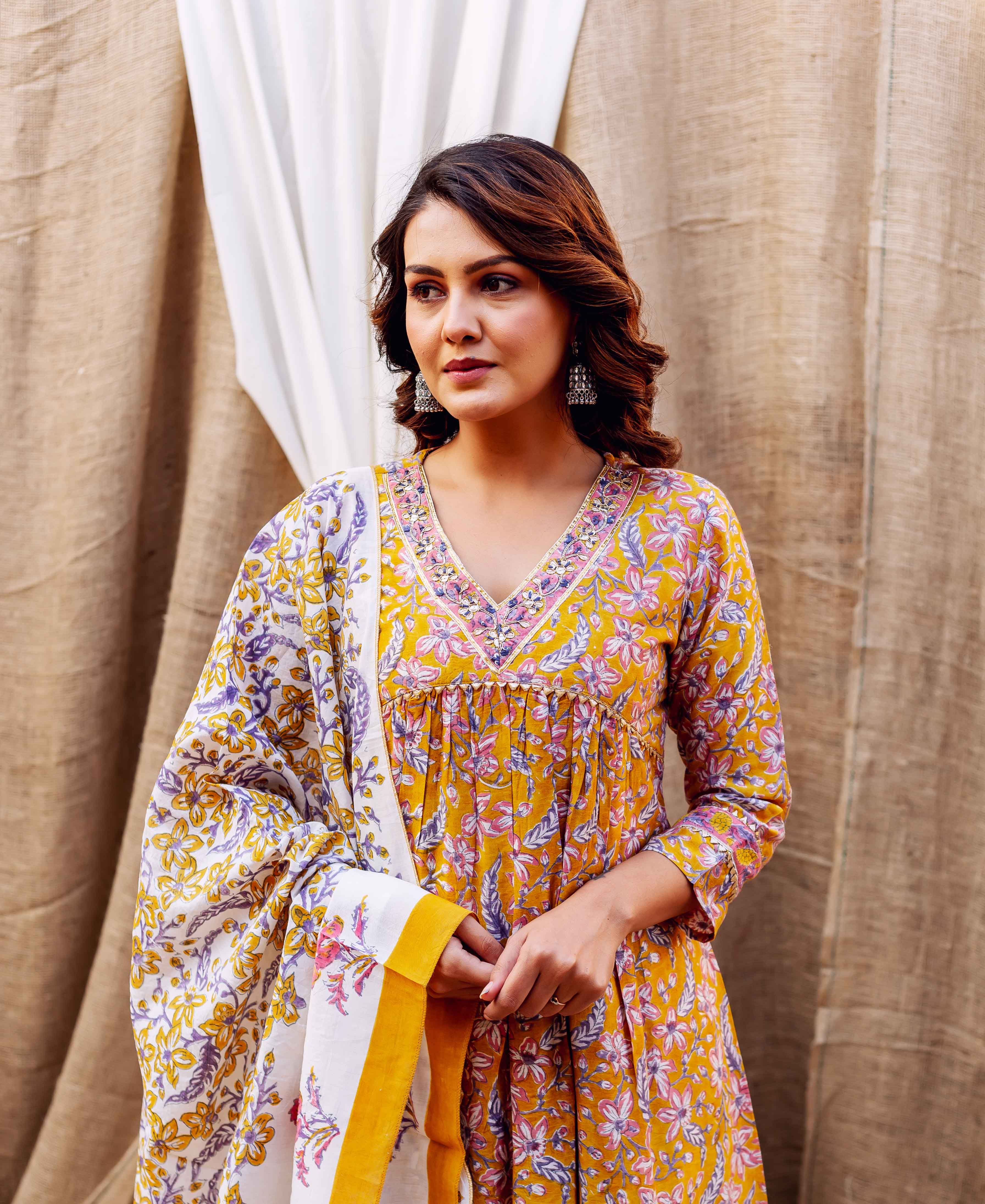 Model wears golden yellow block-printed kurta with pink and purple floral designs, matching dupatta.