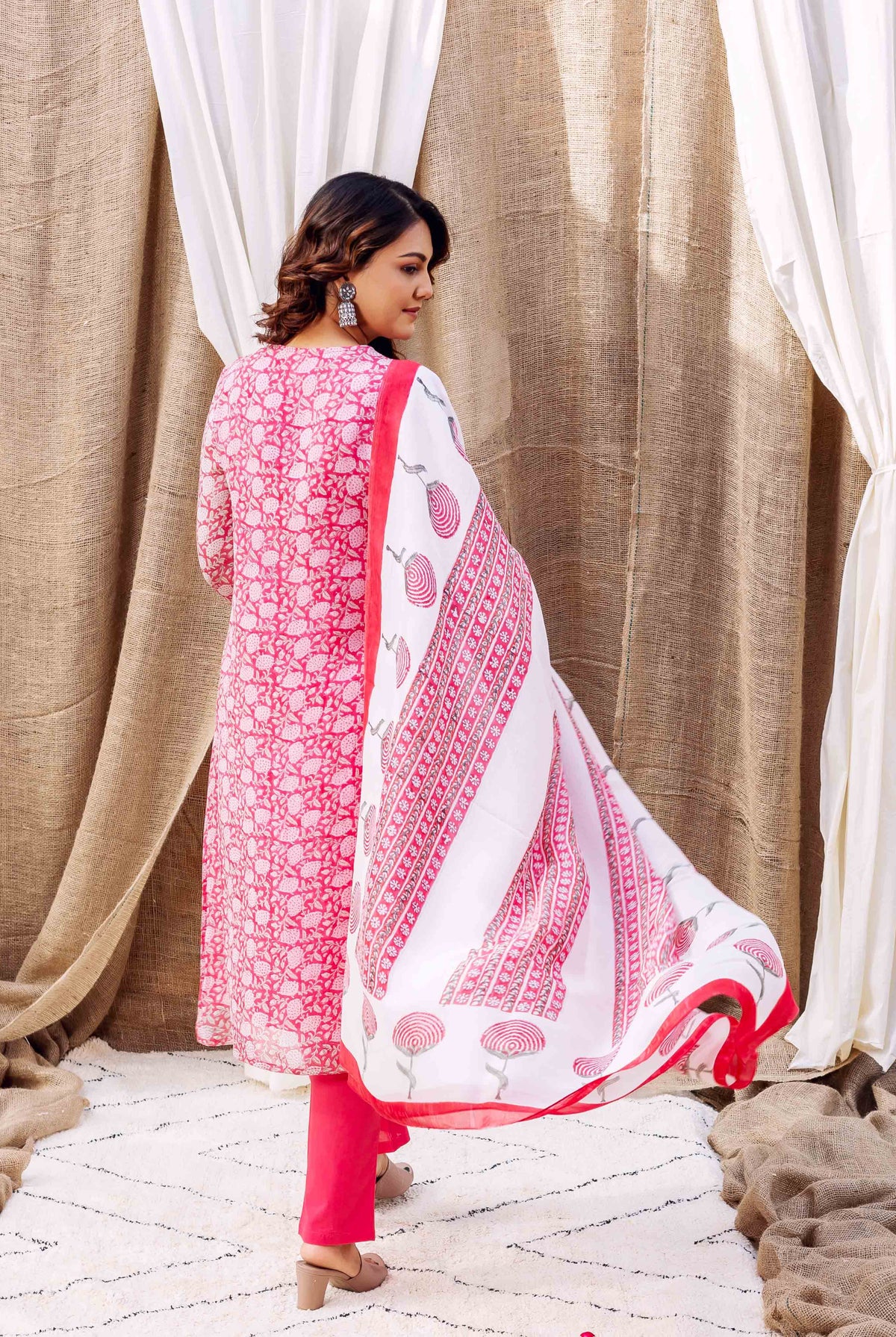 Woman in pink hand-block-printed kurta set with white dupatta, seen from the back.