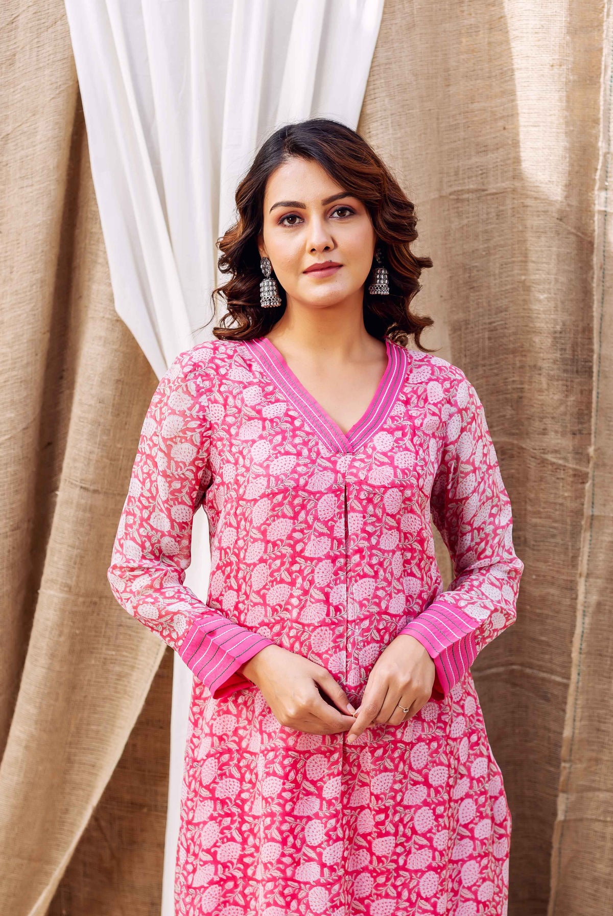 A woman wearing a vibrant pink hand-block-printed kurta with white floral patterns and V-neck.
