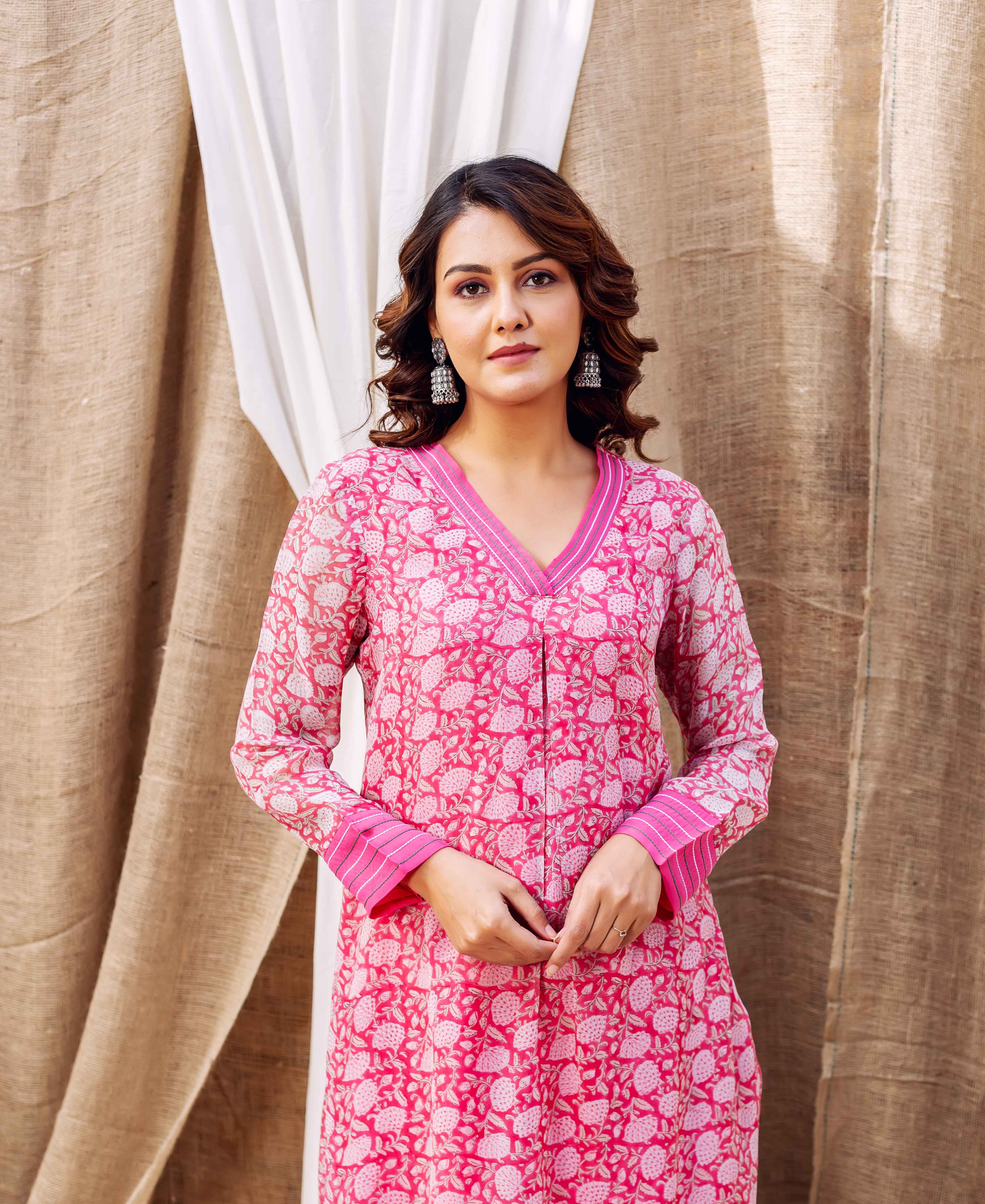 A woman wearing a vibrant pink hand-block-printed kurta with white floral patterns and V-neck.