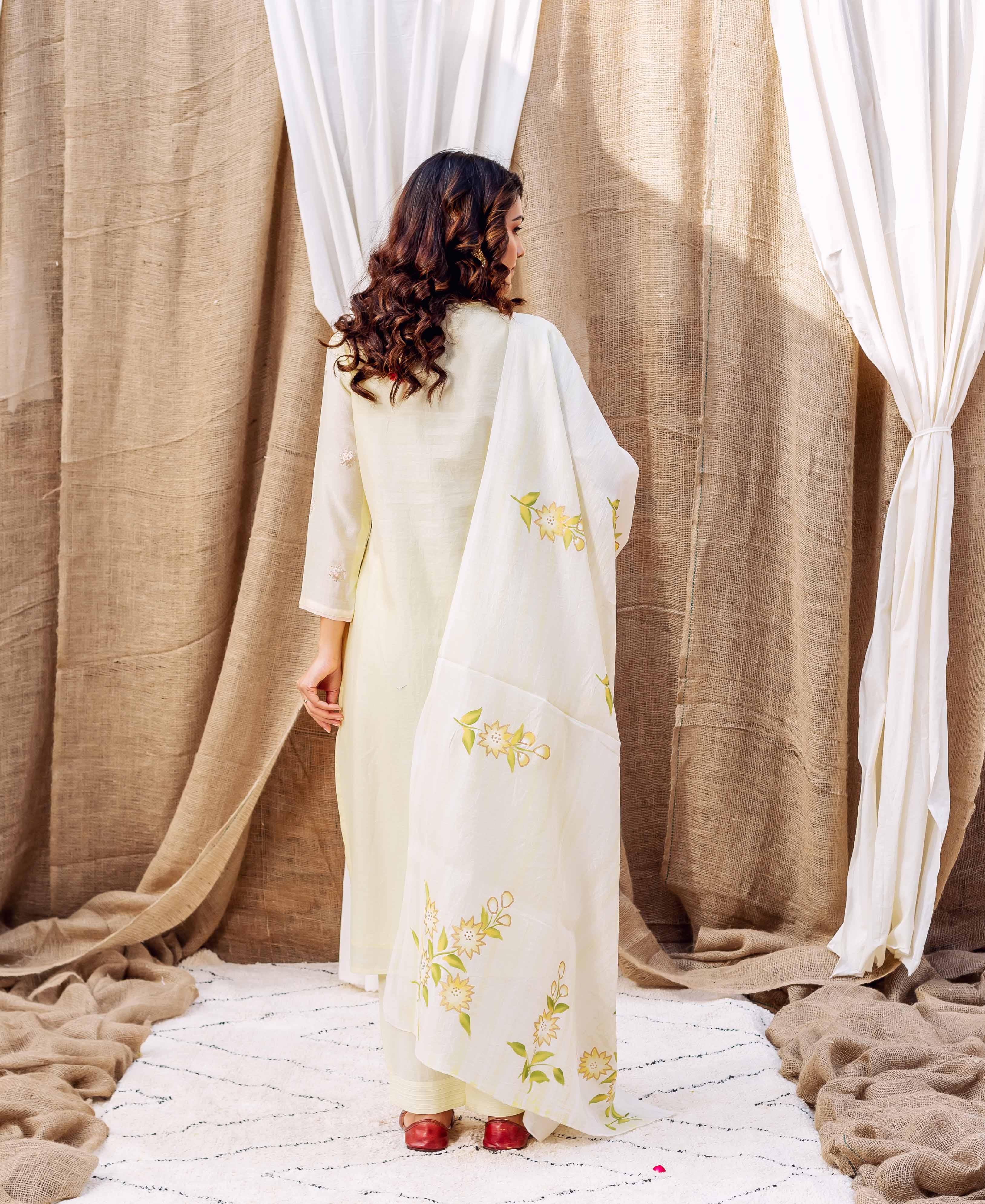 Back view of woman in light yellow kurta and white dupatta with green-yellow floral print.