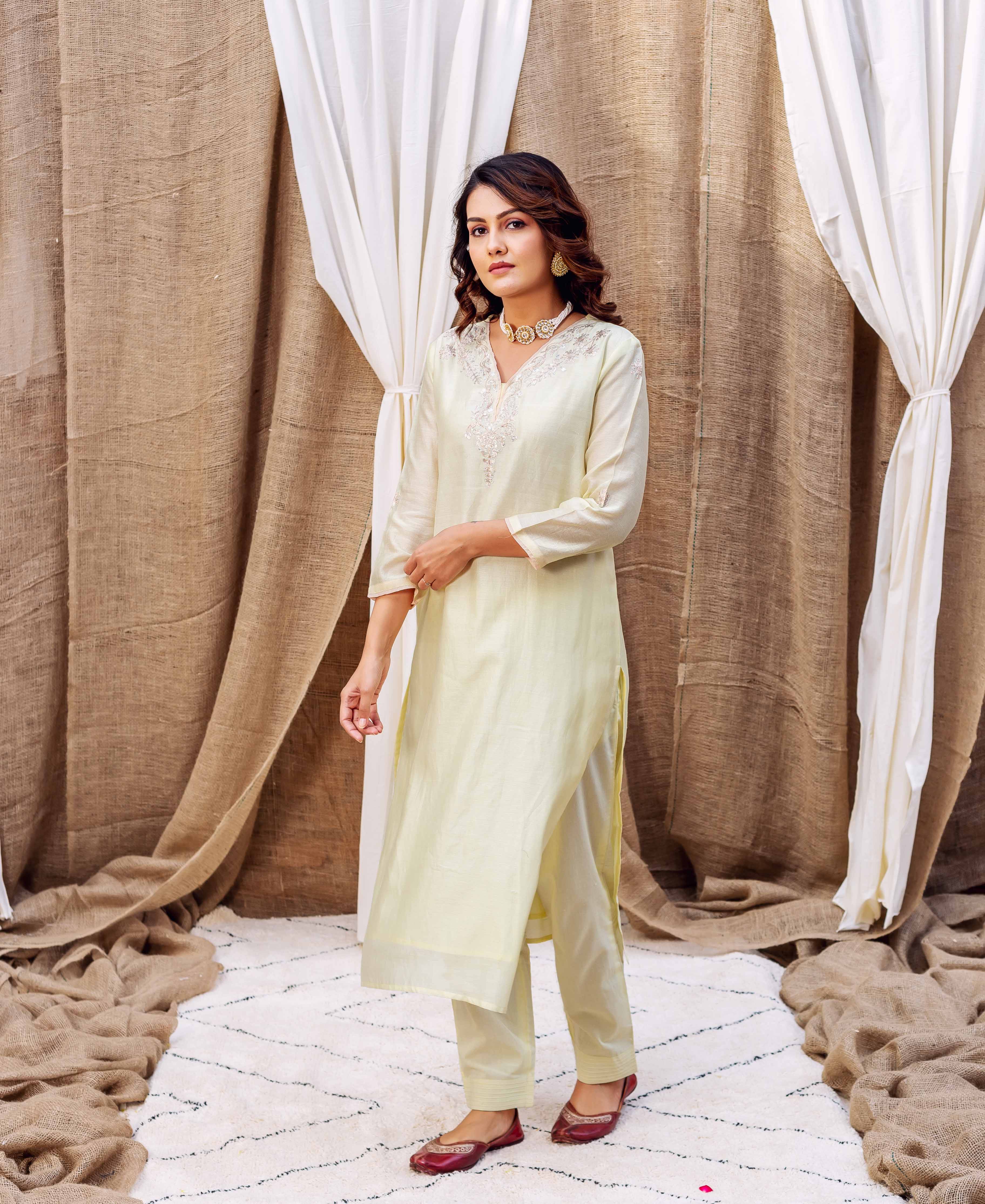 Model in pale yellow kurta set with intricate white embroidered V-neckline and matching pants.