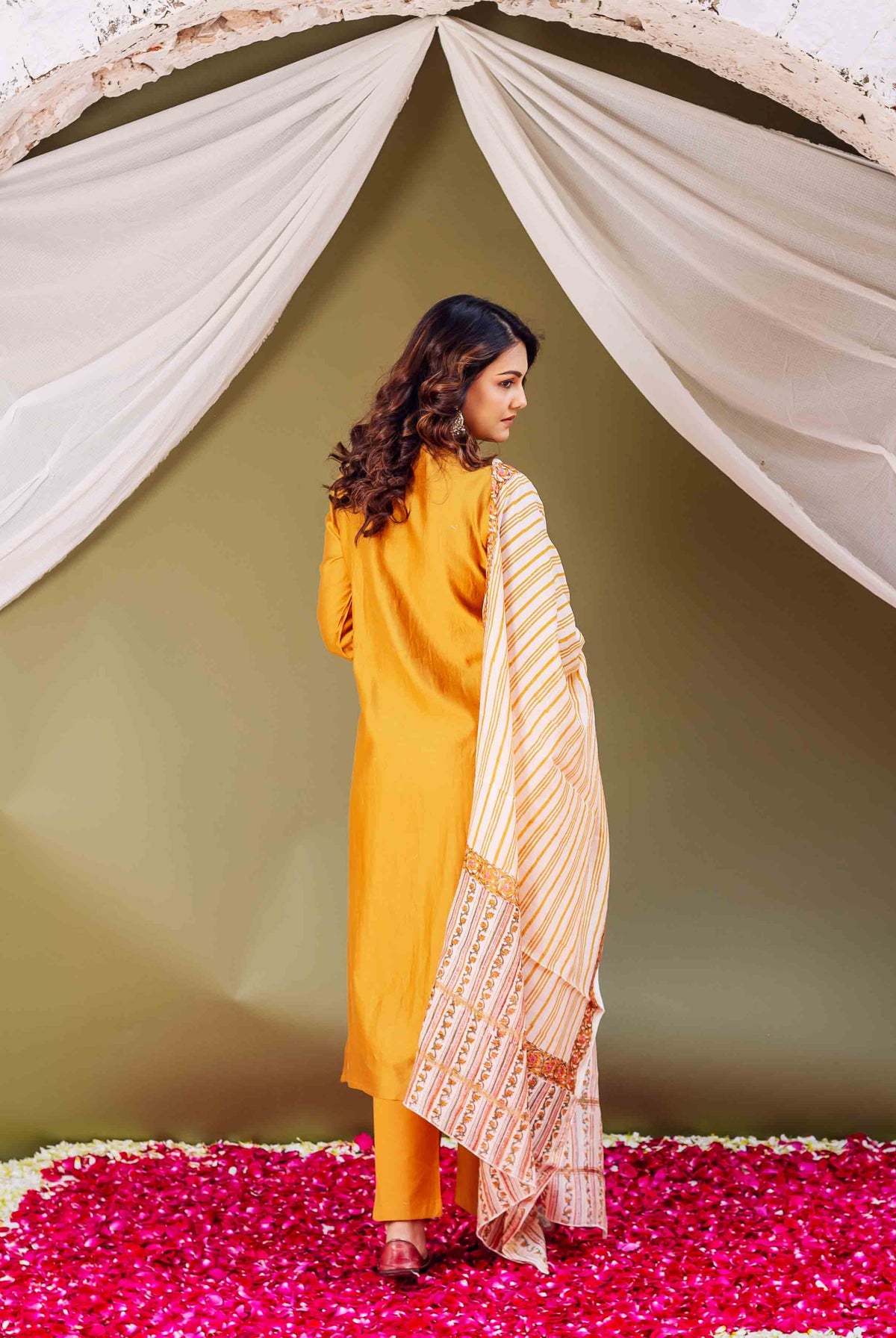 Model from back in mustard silk kurta and white striped dupatta with patterned border.