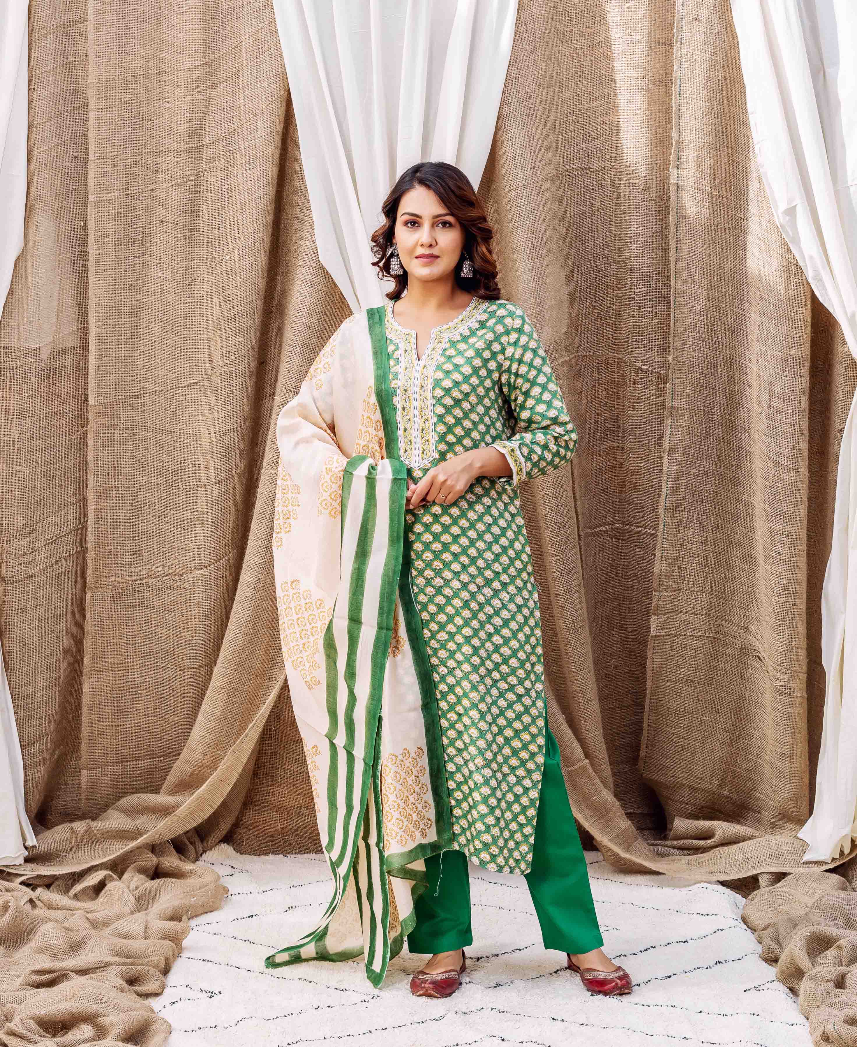 Woman standing in a green booti printed kurta, plain green pants, and striped cream dupatta.