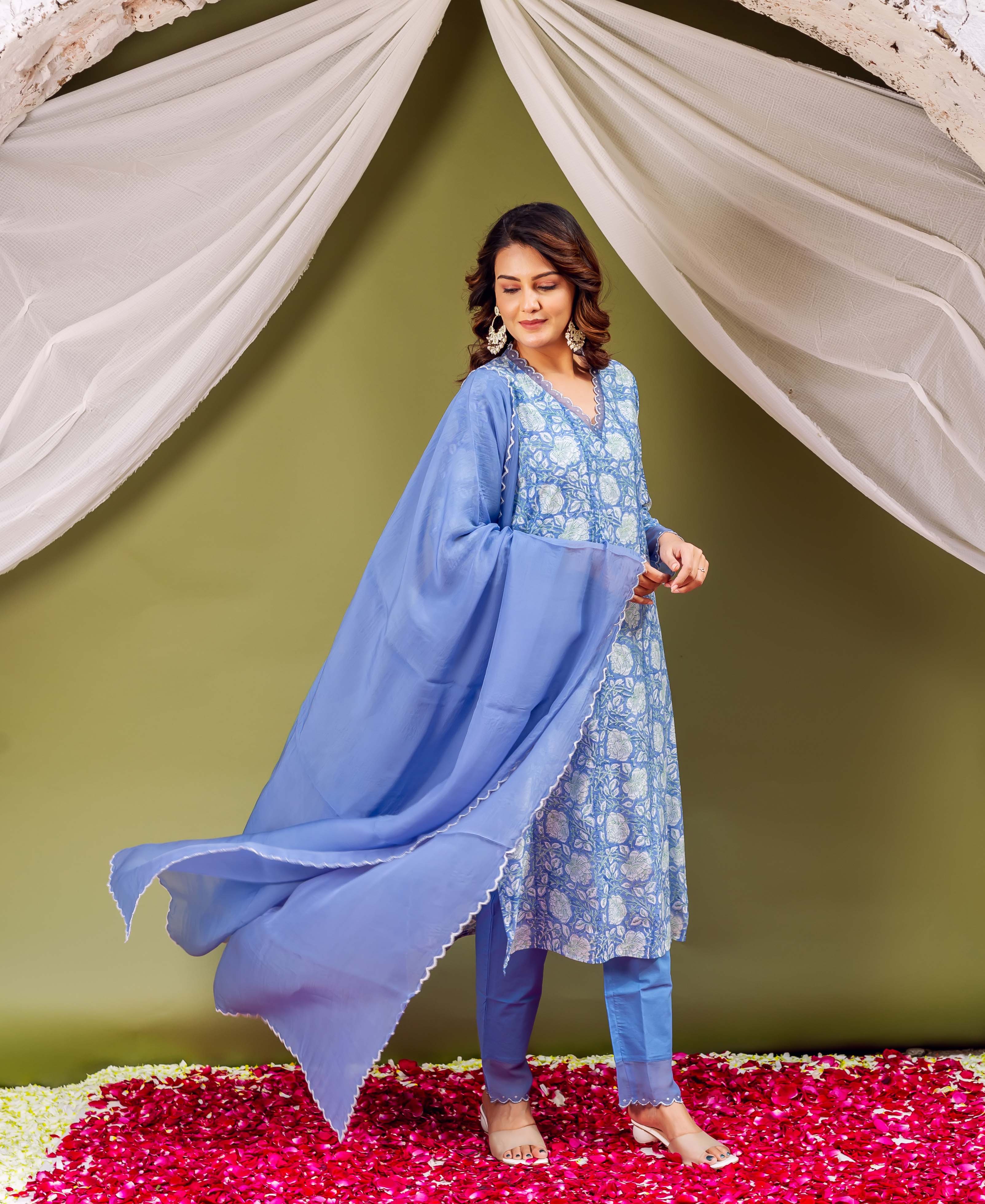 Woman in blue outfit with white floral pattern and azure dupatta flowing beside her.