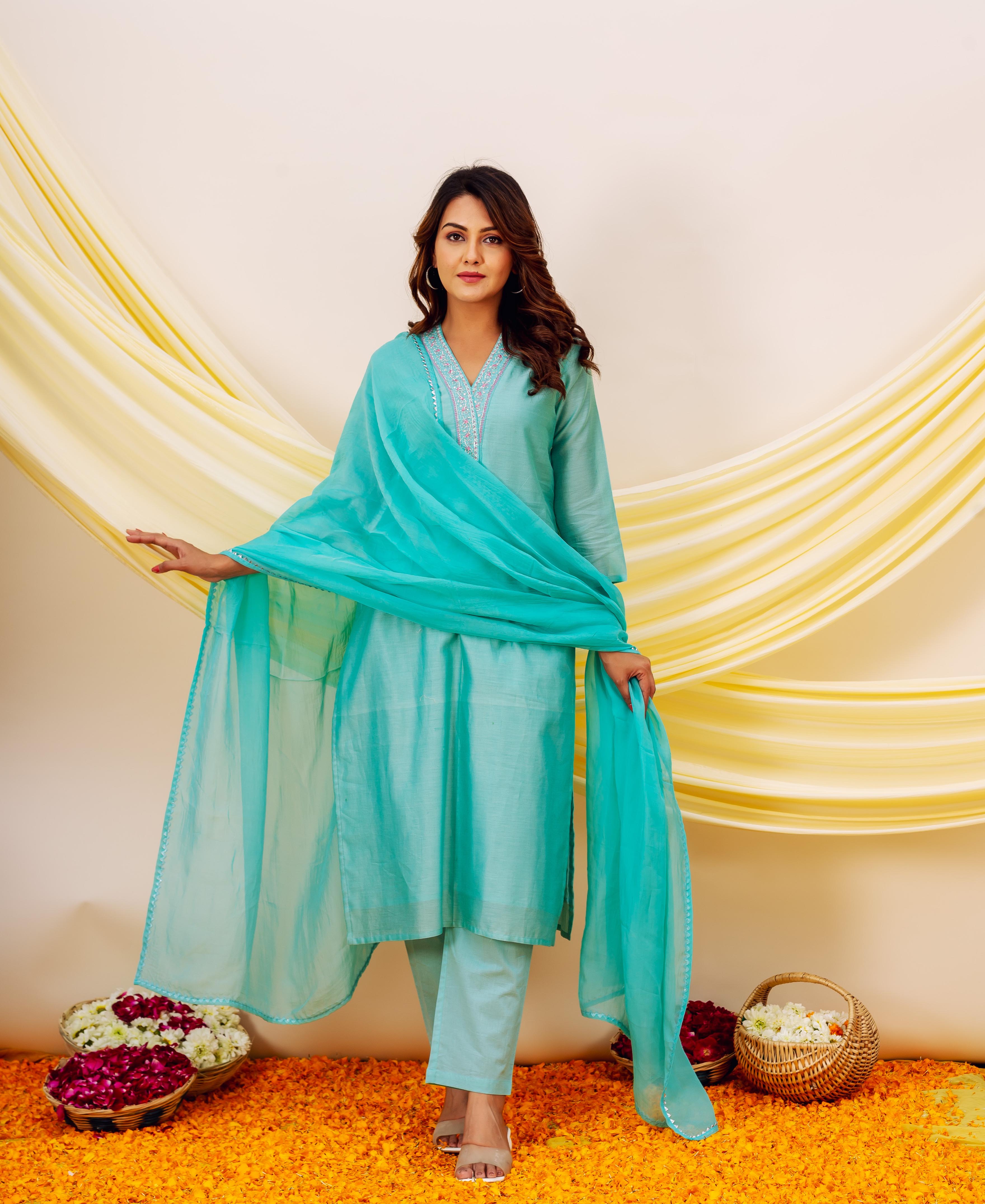 Turquoise outfit with sheer aqua dupatta and embroidered neckline, model standing on orange flower petals.