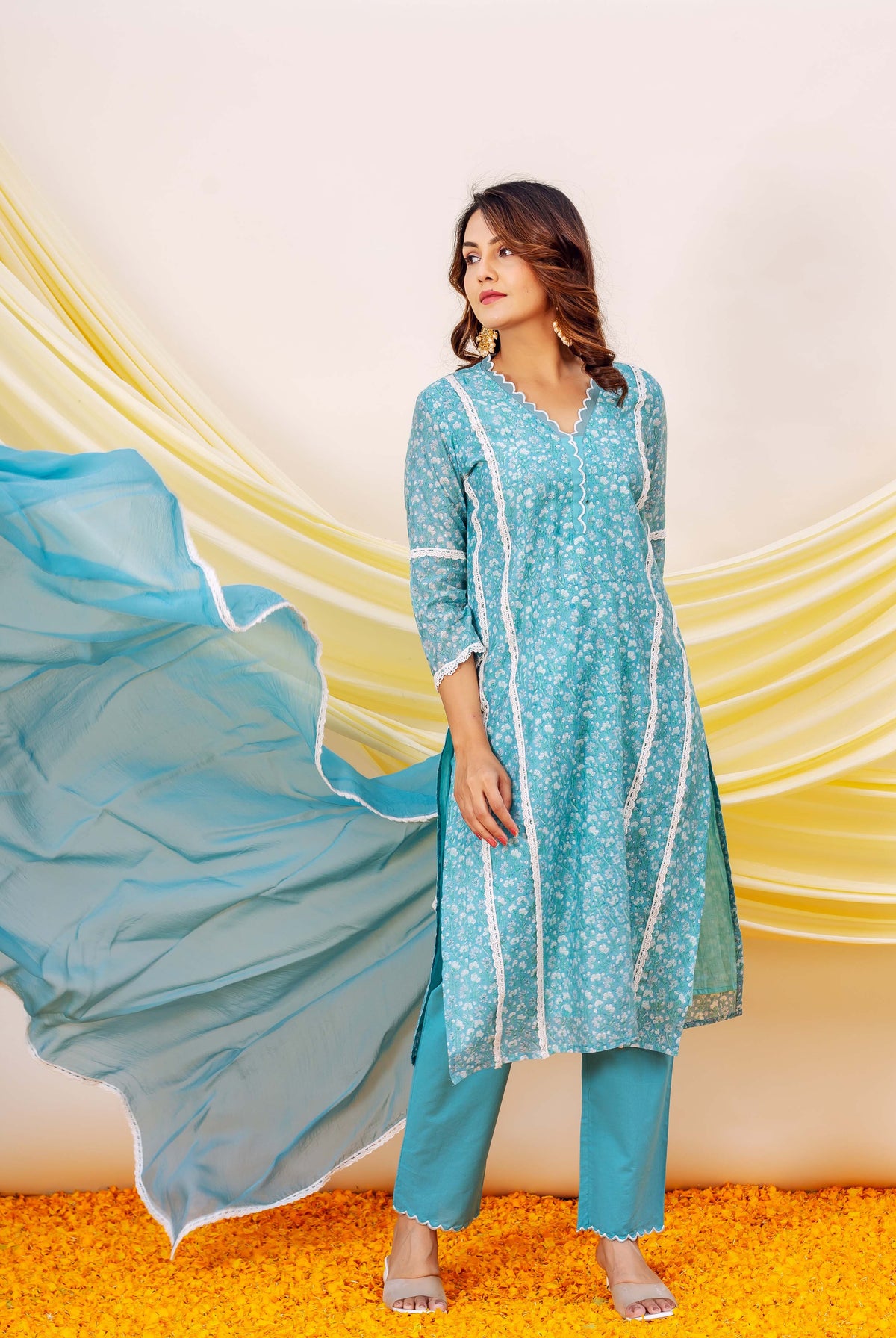 Model wearing a blue hand block printed floral kurta set with white lace and flowing dupatta.