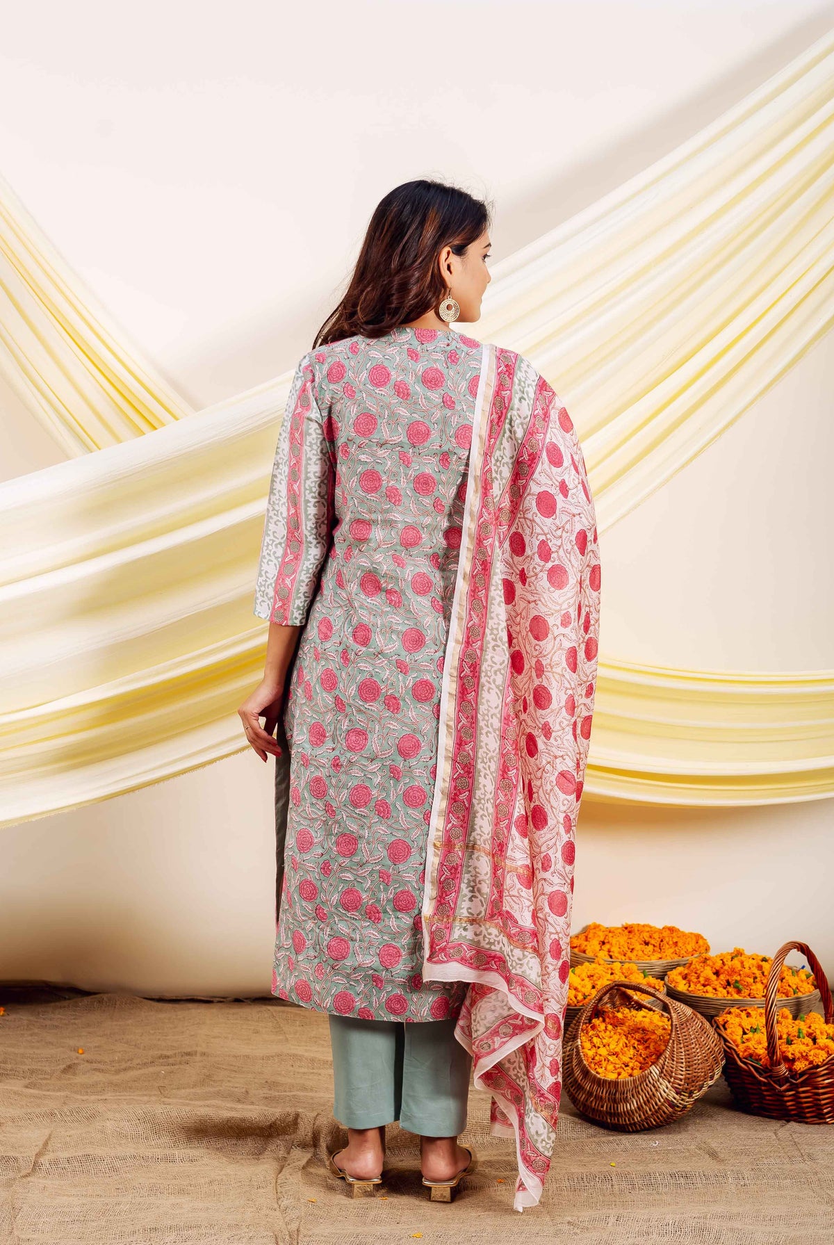 Woman from back in grey-green block-printed suit with pink florals and draped dupatta.
