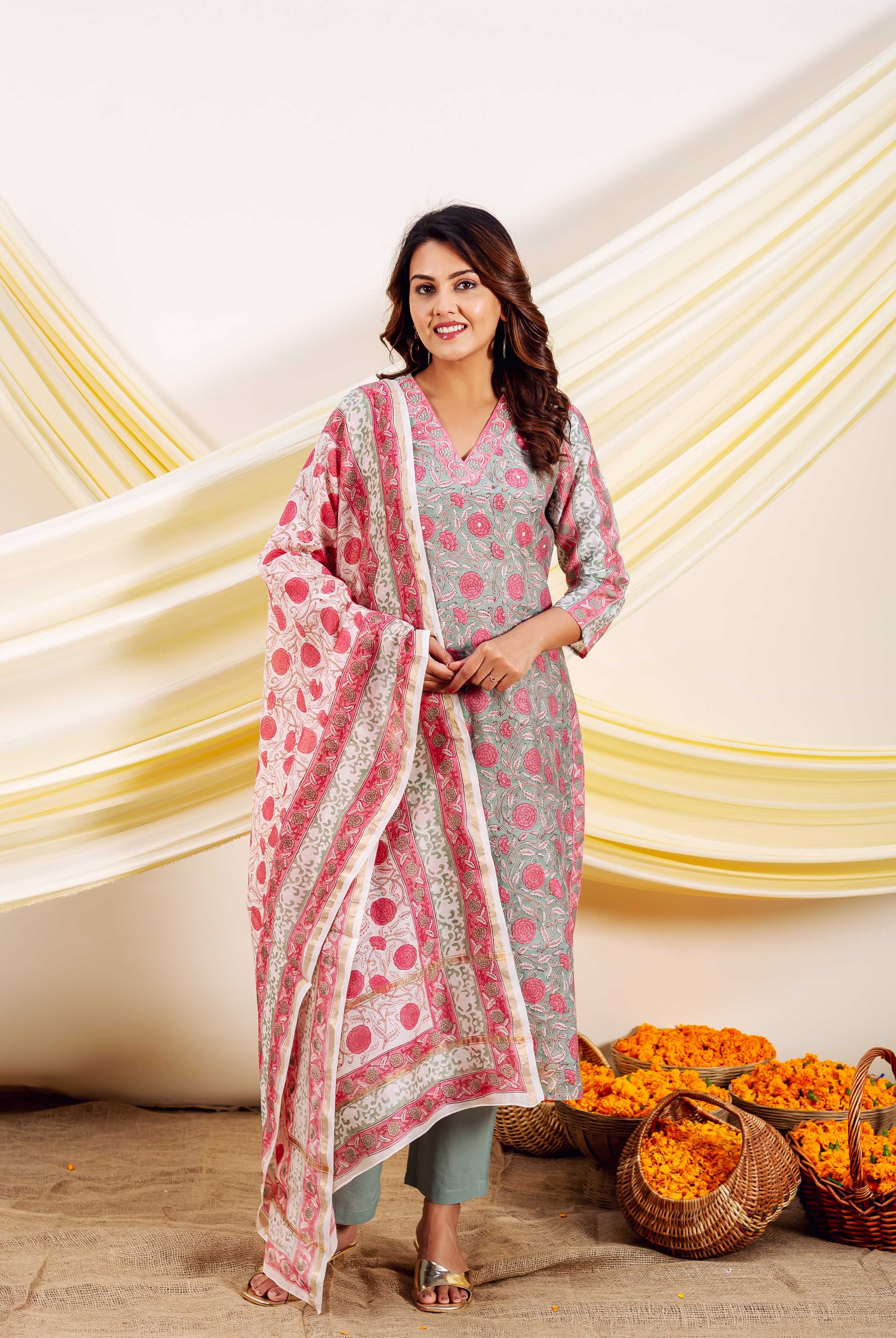 Smiling woman in grey and pink floral block-printed kurta, green pants, and white dupatta.