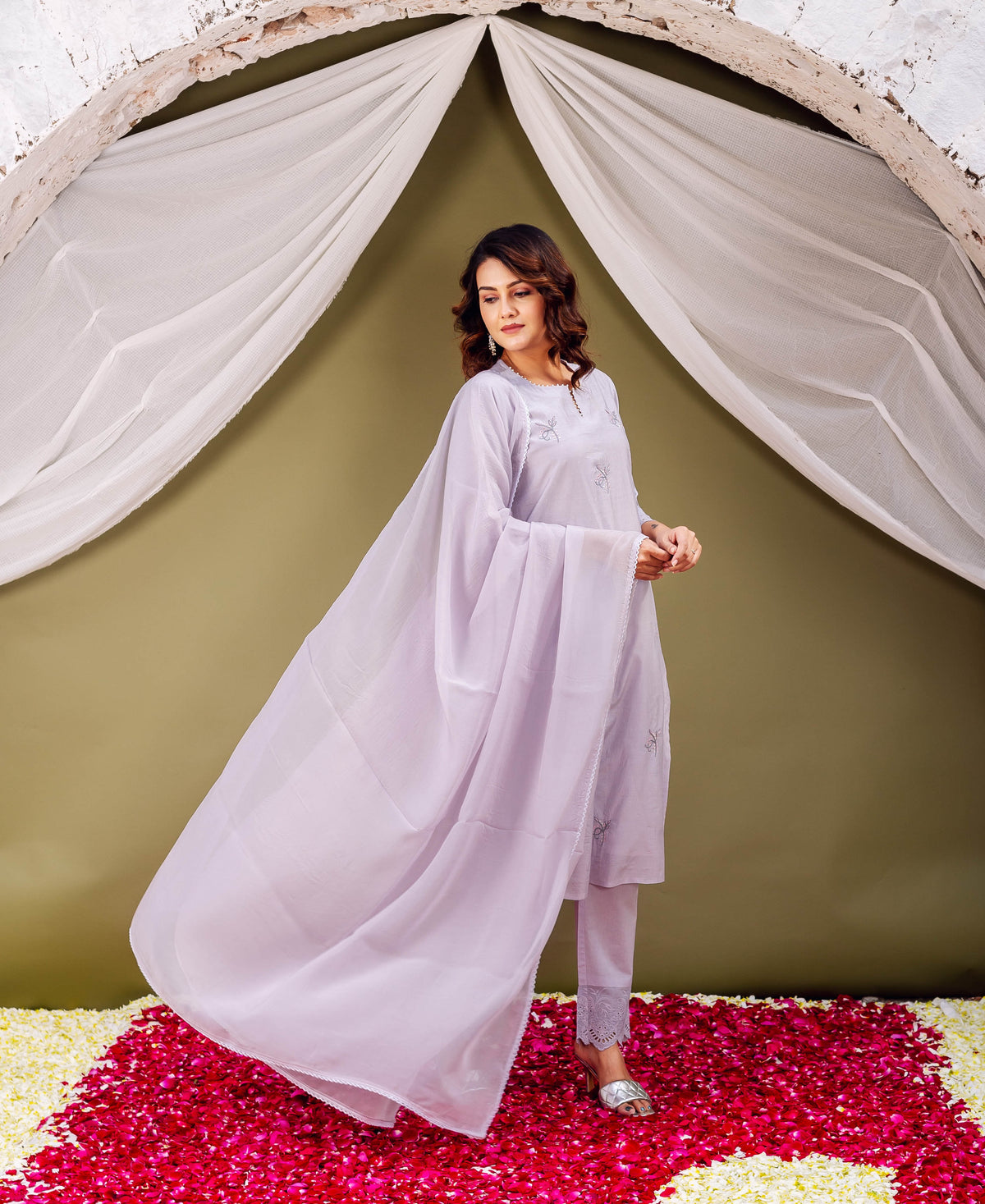 A woman in a lavender chanderi silk kurta with floral print, standing on rose petals.