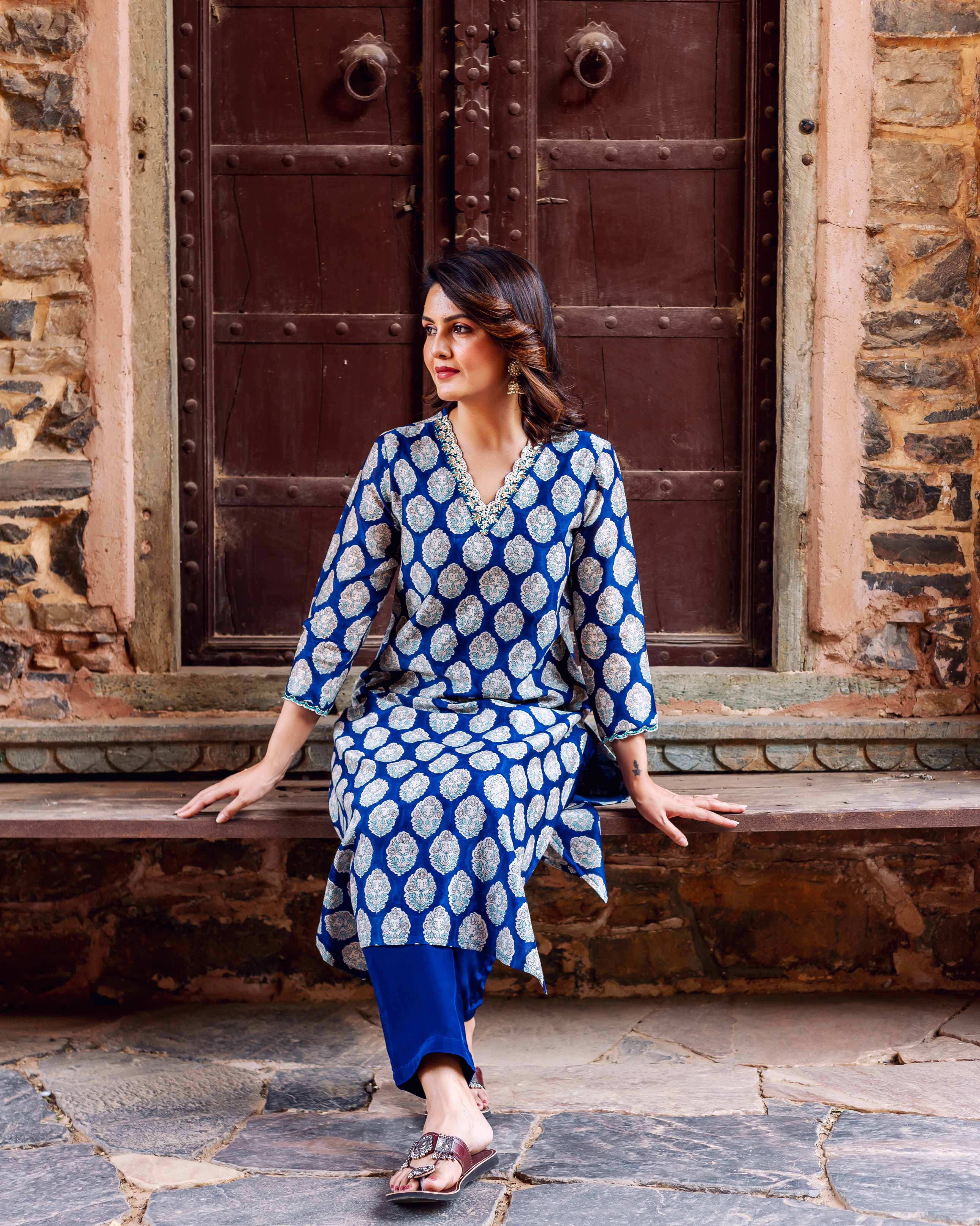 Model wearing an indigo blue booti print chanderi silk kurta set, sitting on a stone bench.