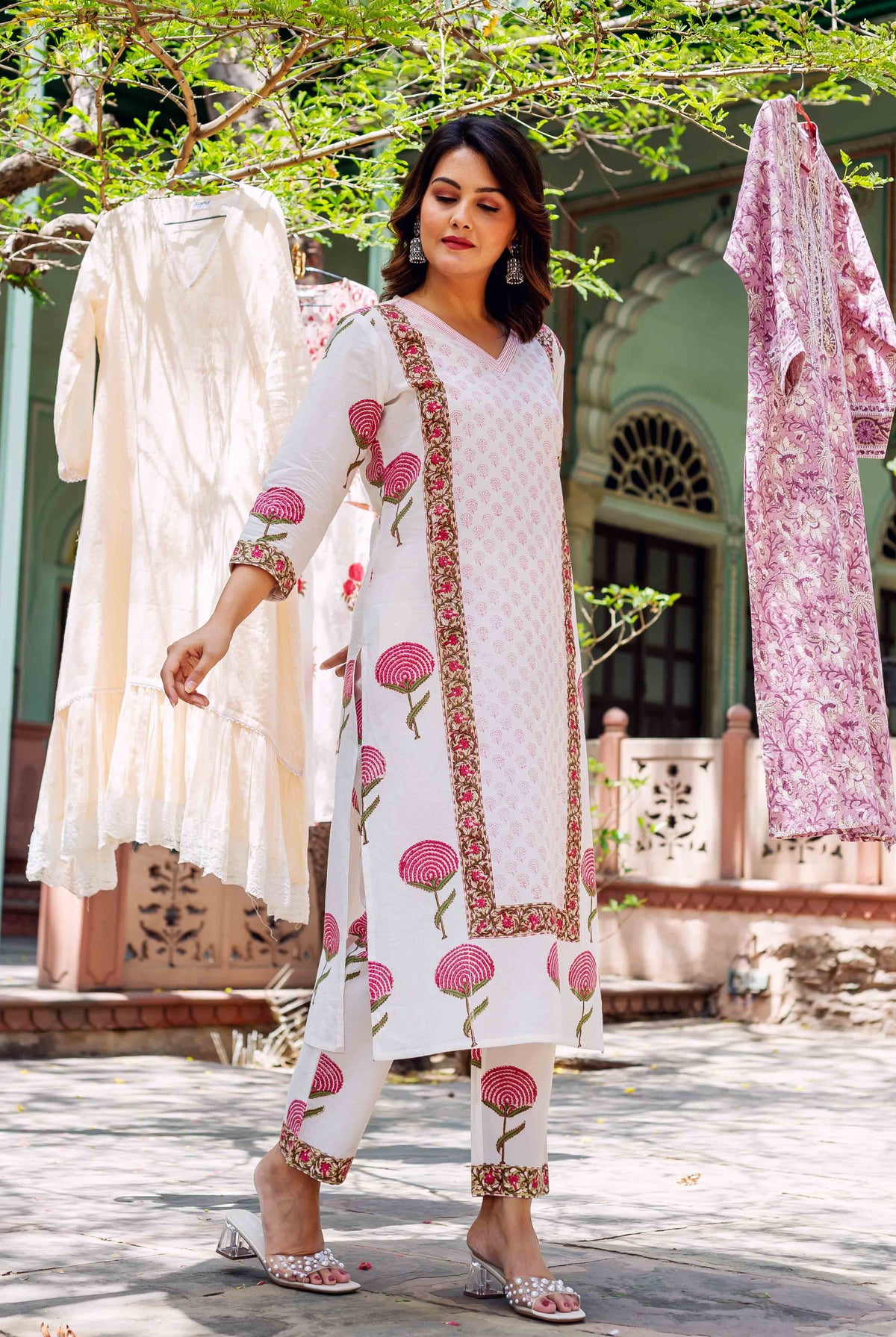 Woman wears white hand-block-printed cotton kurta set with pink floral motifs, standing outdoors.