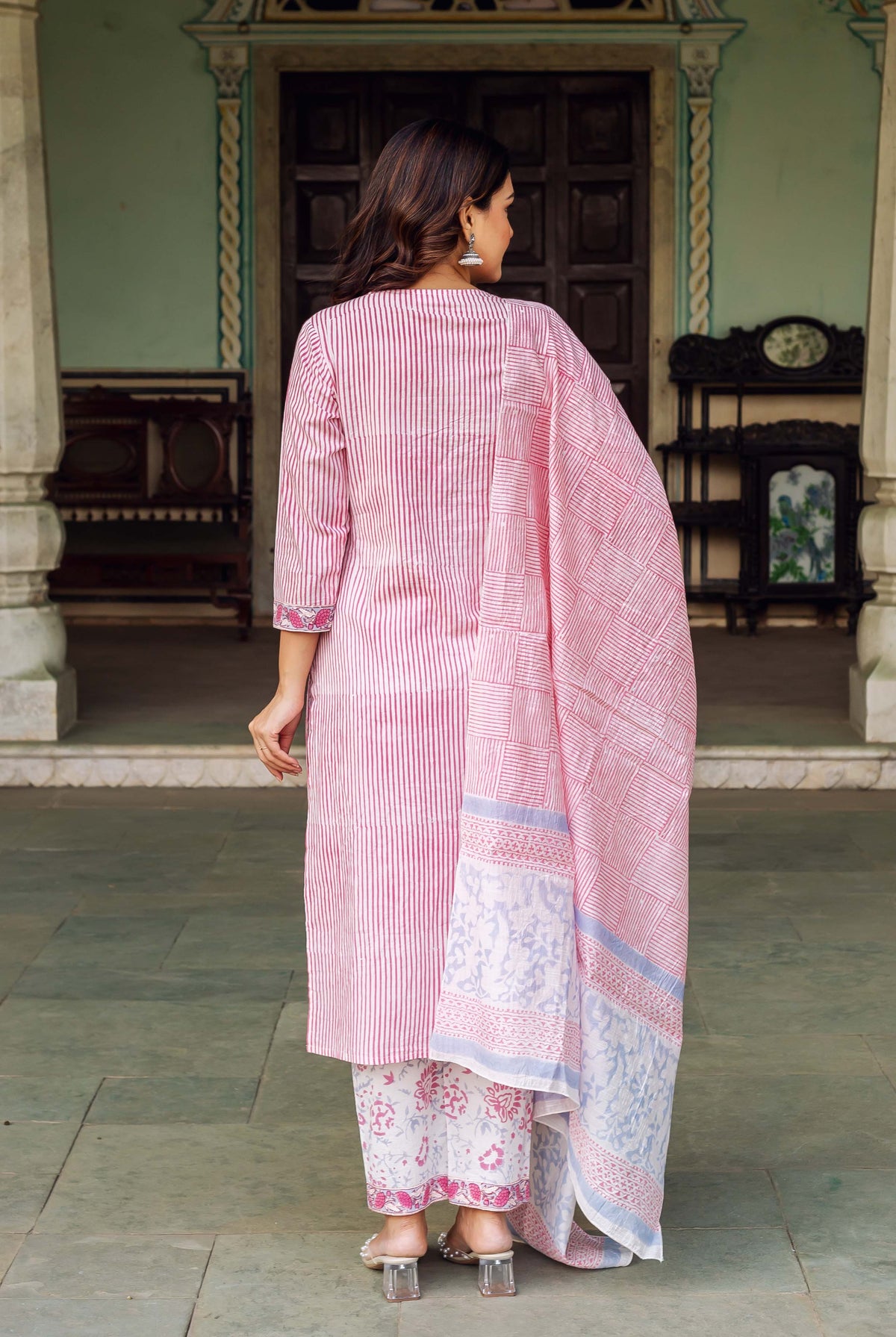 Woman in pink and white striped kurta and patterned pants with long dupatta.