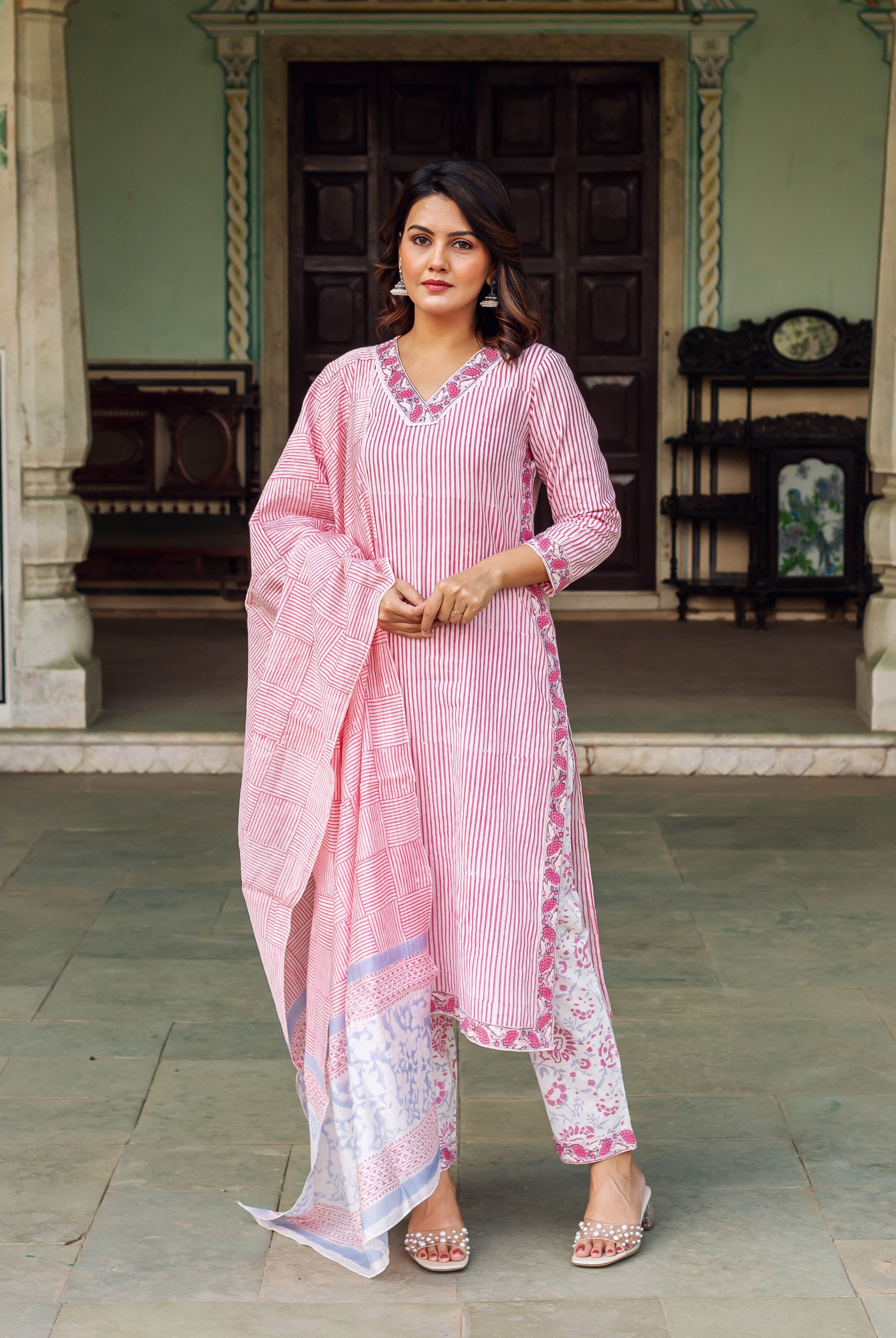 Full body shot of a woman modeling a white and pink striped kurta set with floral accents.