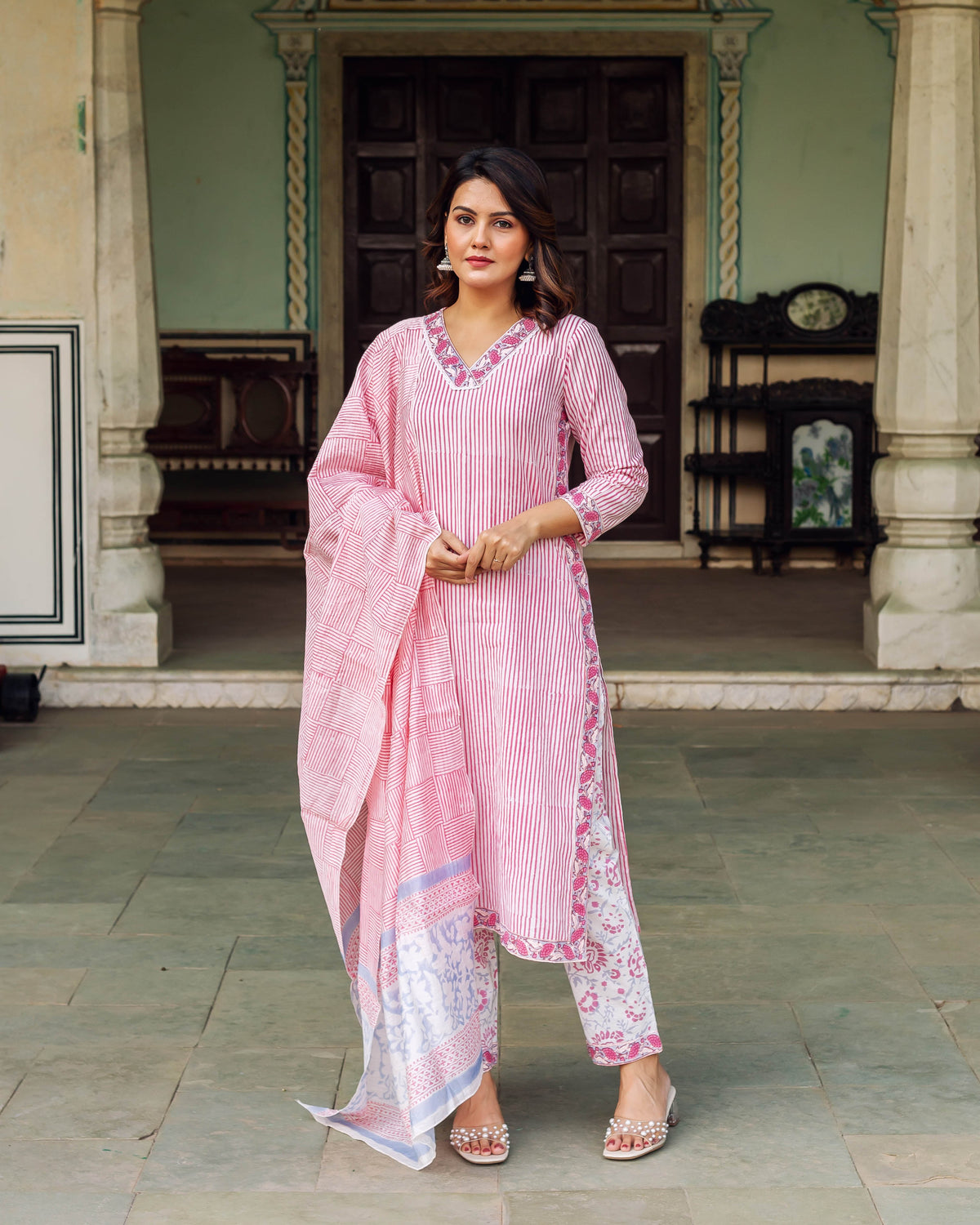 Full body shot of a woman modeling a white and pink striped kurta set with floral accents.