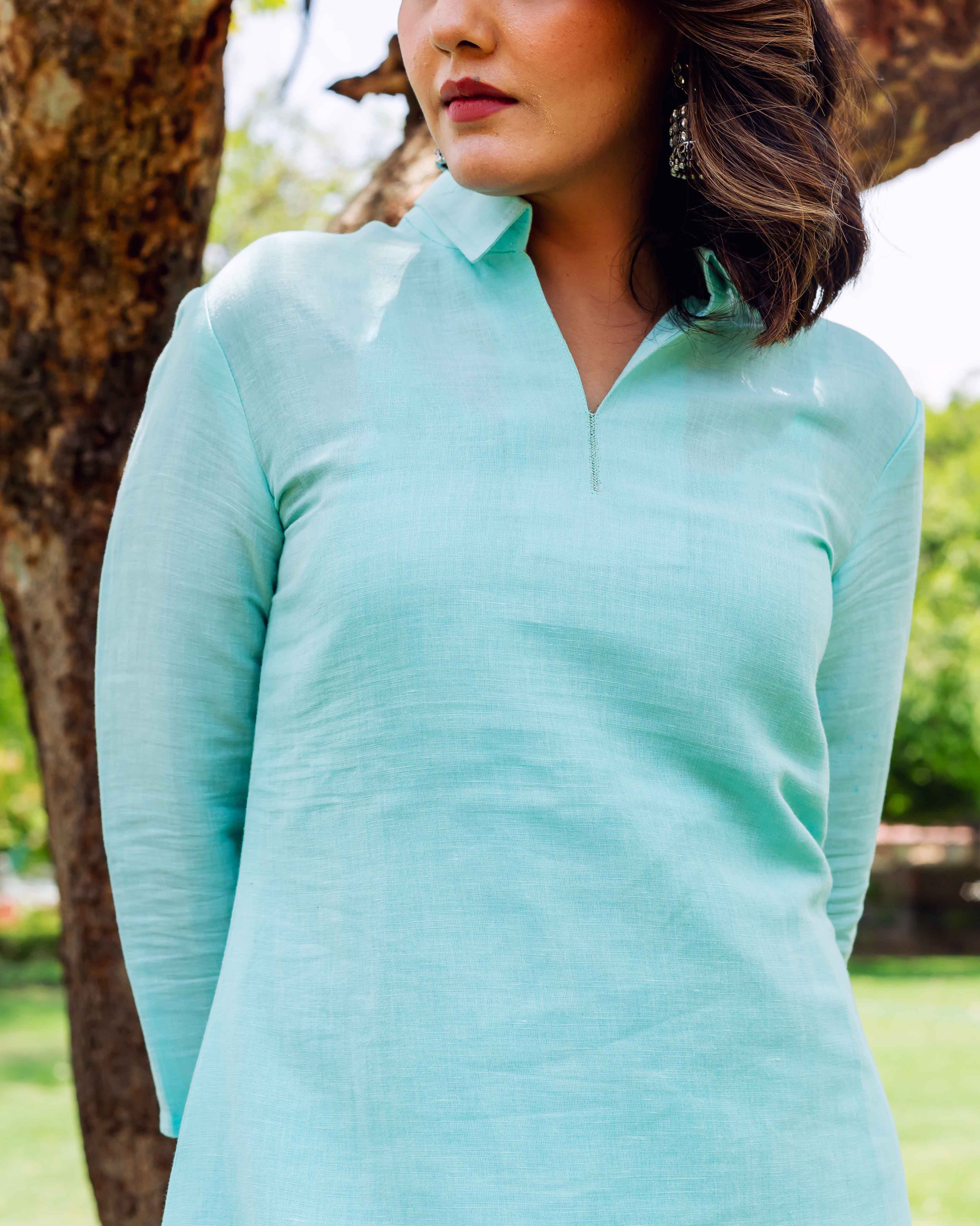 Model wearing a bright sky blue linen top with a collar and stitched V-neck.