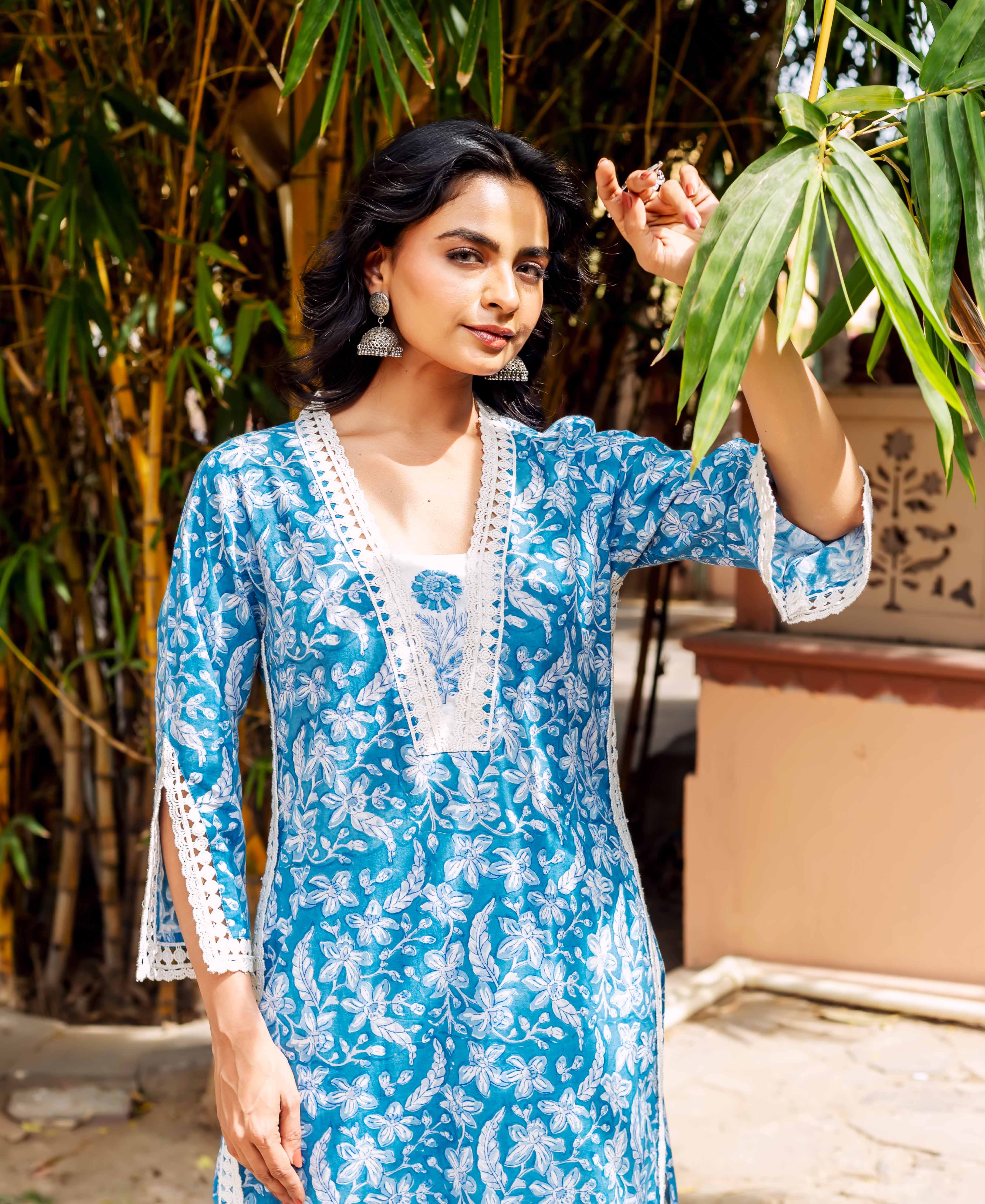 Model poses in blue floral cotton kurta, detailed with white lace on neckline and sleeves.