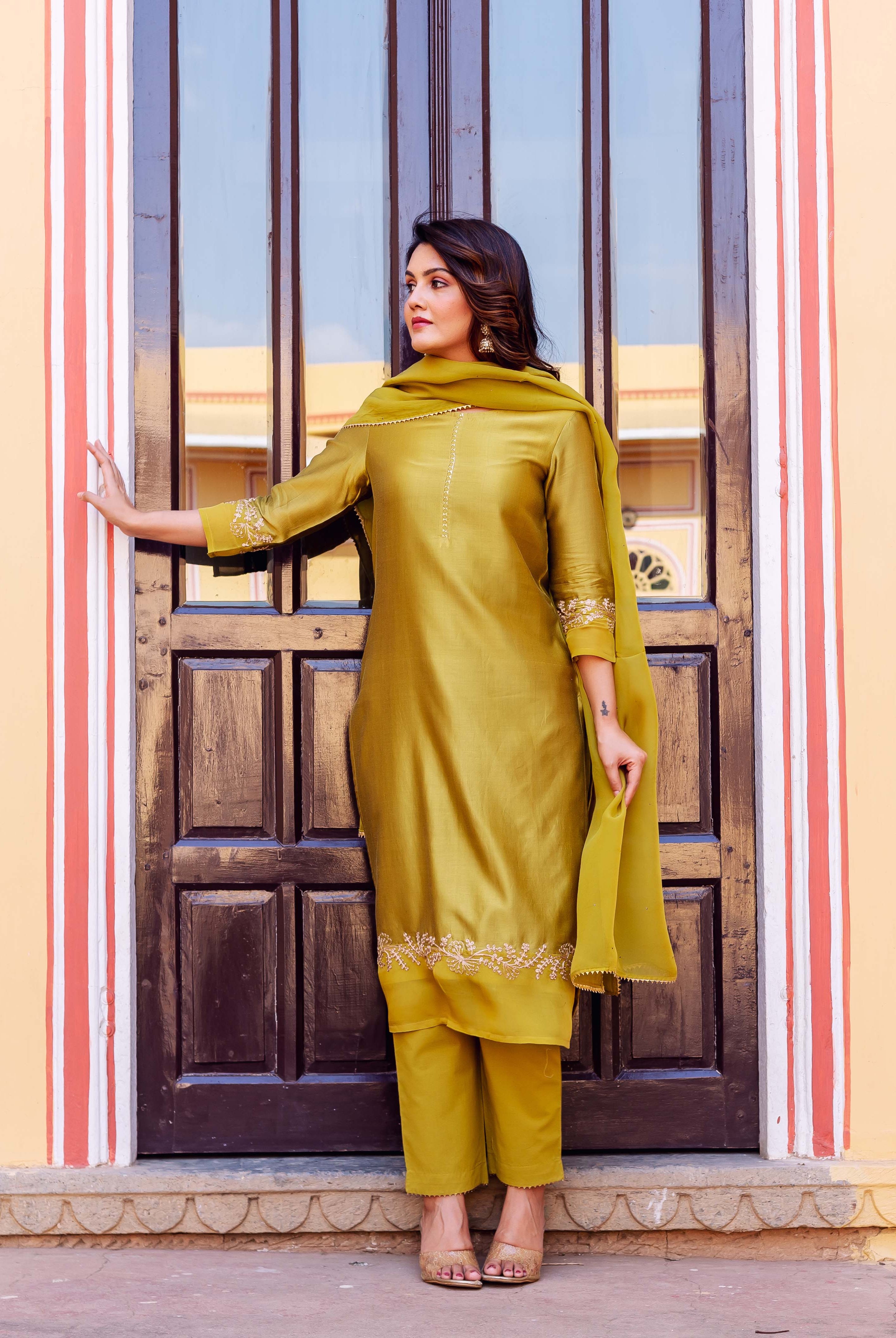 A woman in a yellow kurta with white embroidery, standing in front of a door.
