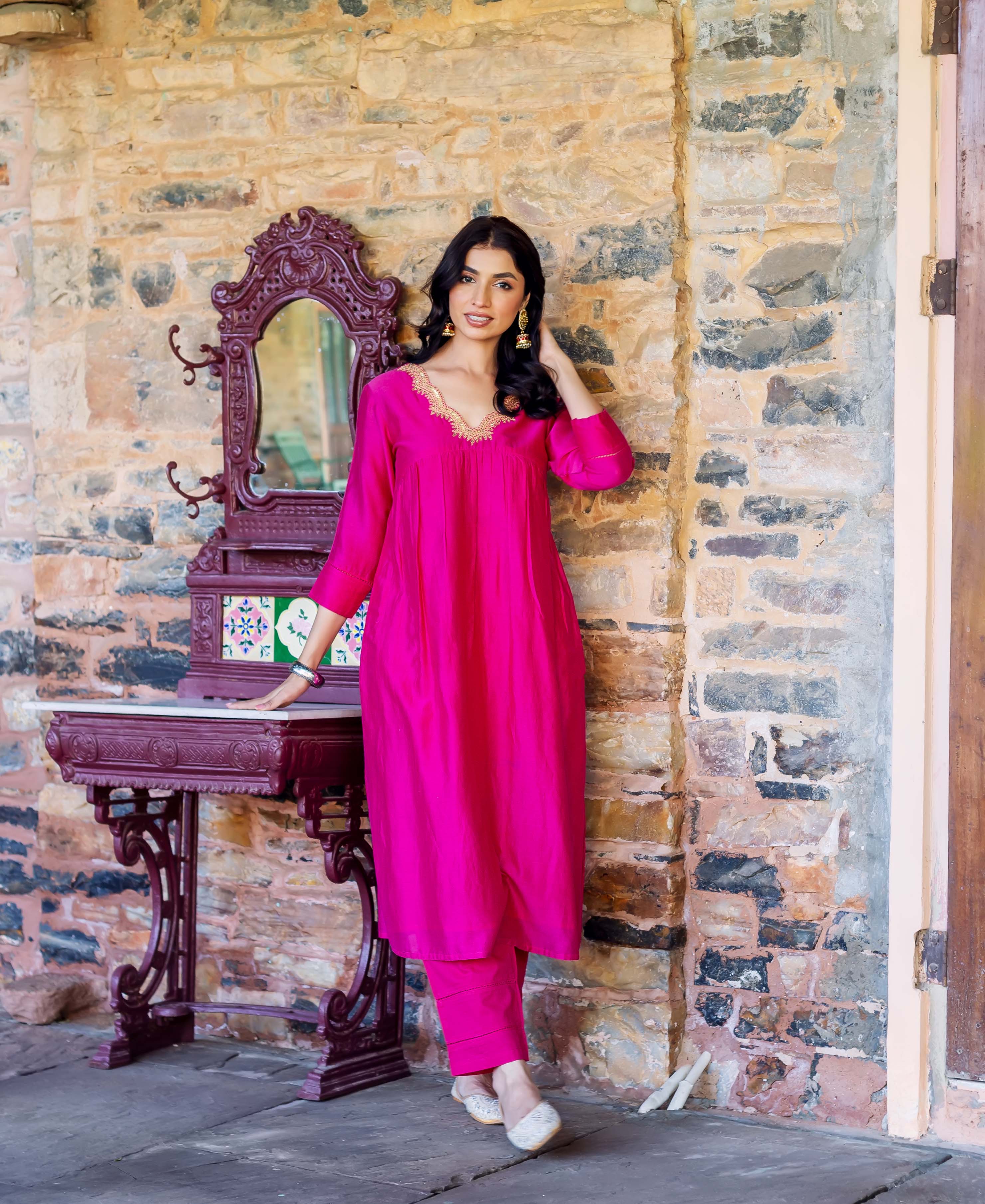 Model wears a radiant pink Chanderi silk kurta featuring an embroidered gold V-neck and matching pants.