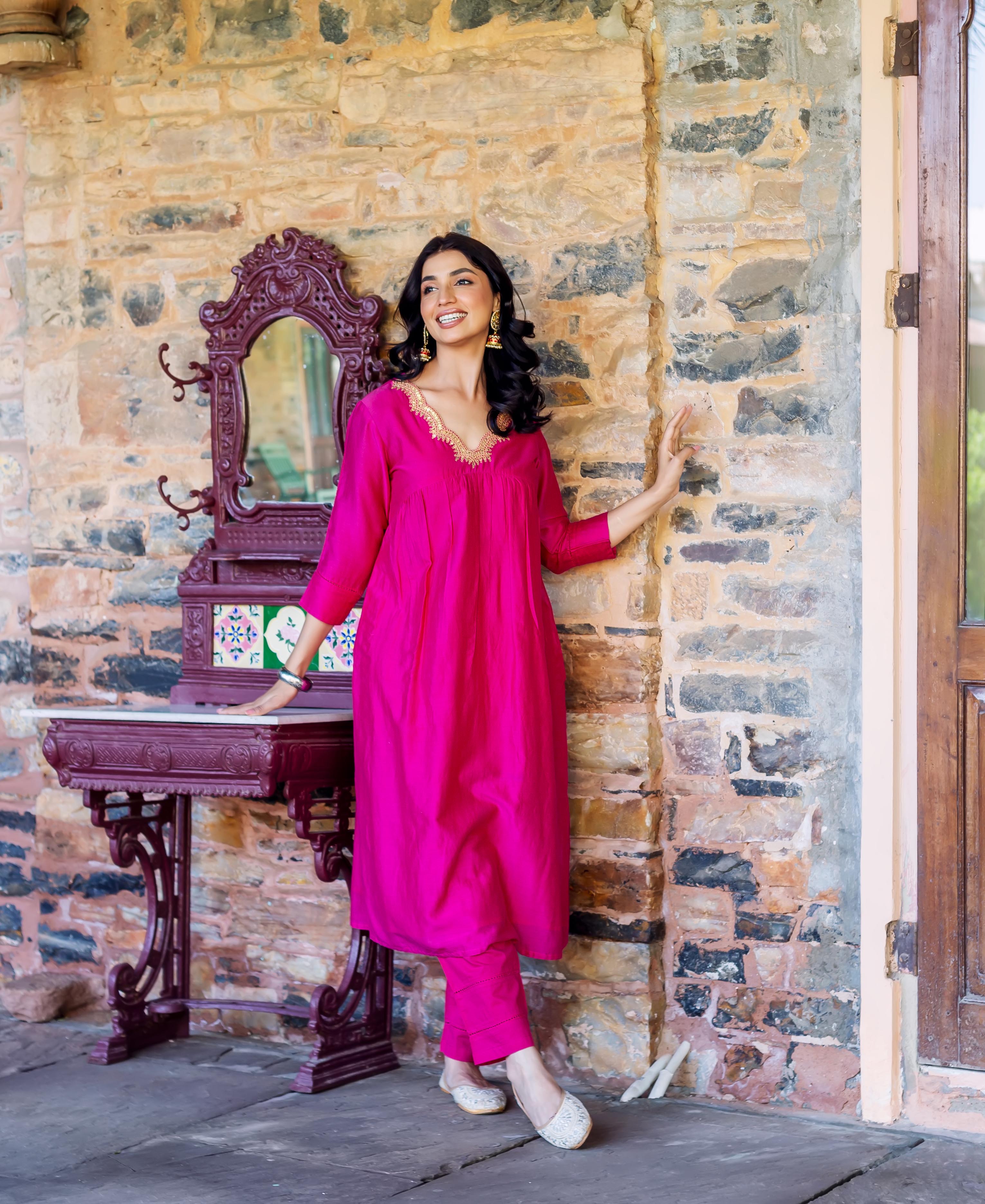 Full-length photo of a woman wearing a radiant pink kurta set with golden embroidered neckline.