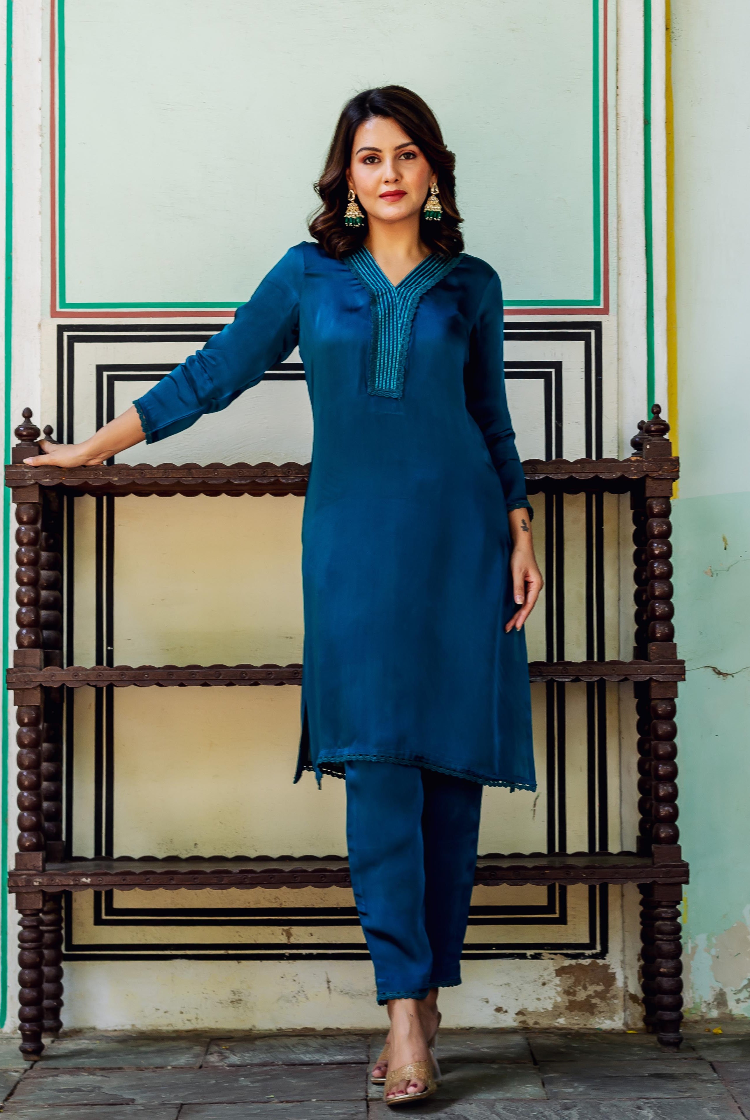 Model posing in a royal blue satin kurta set with teal embroidered V-neck.