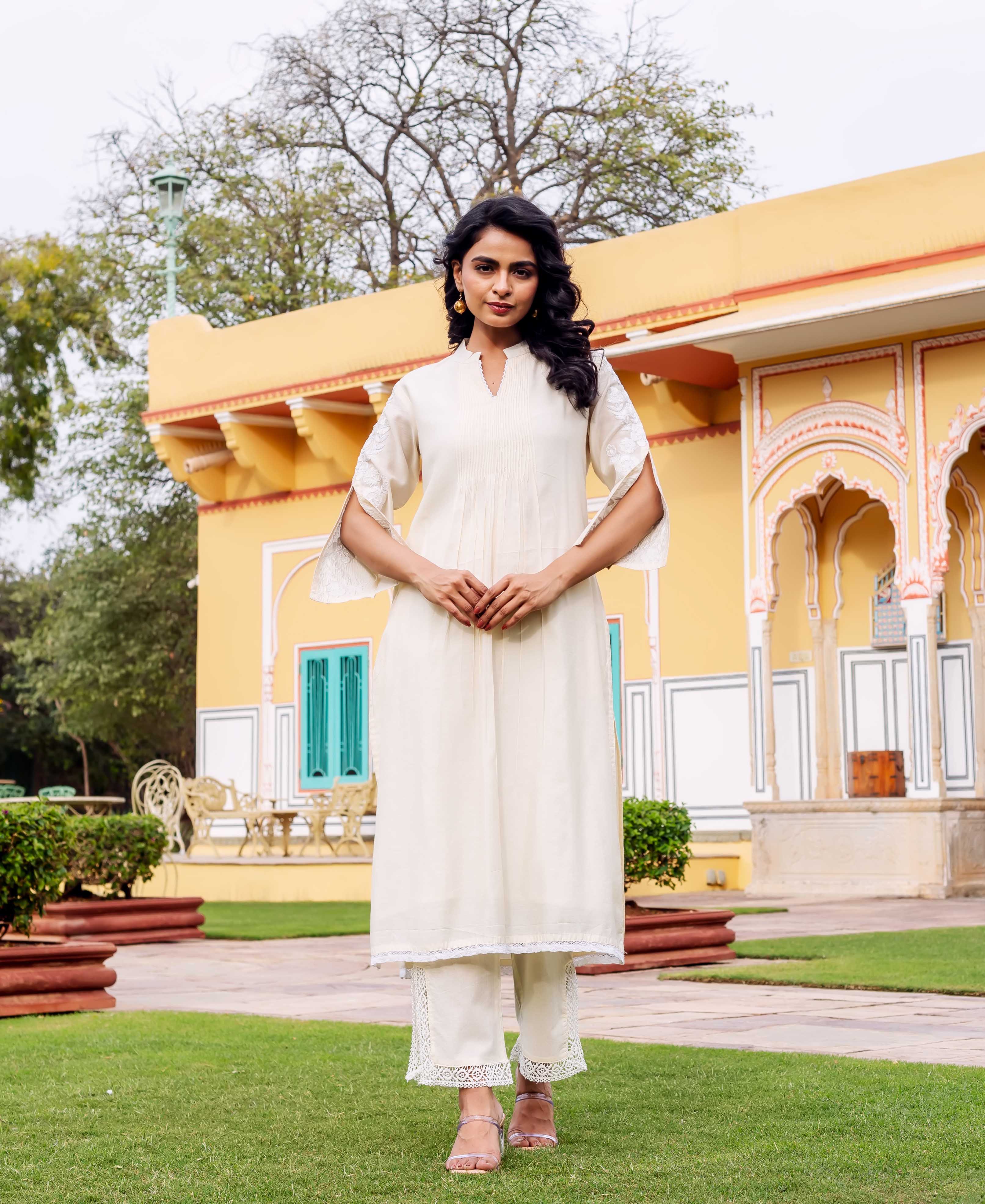 Model wearing antique white pleated kurta set with embroidered split sleeves and lace hems.