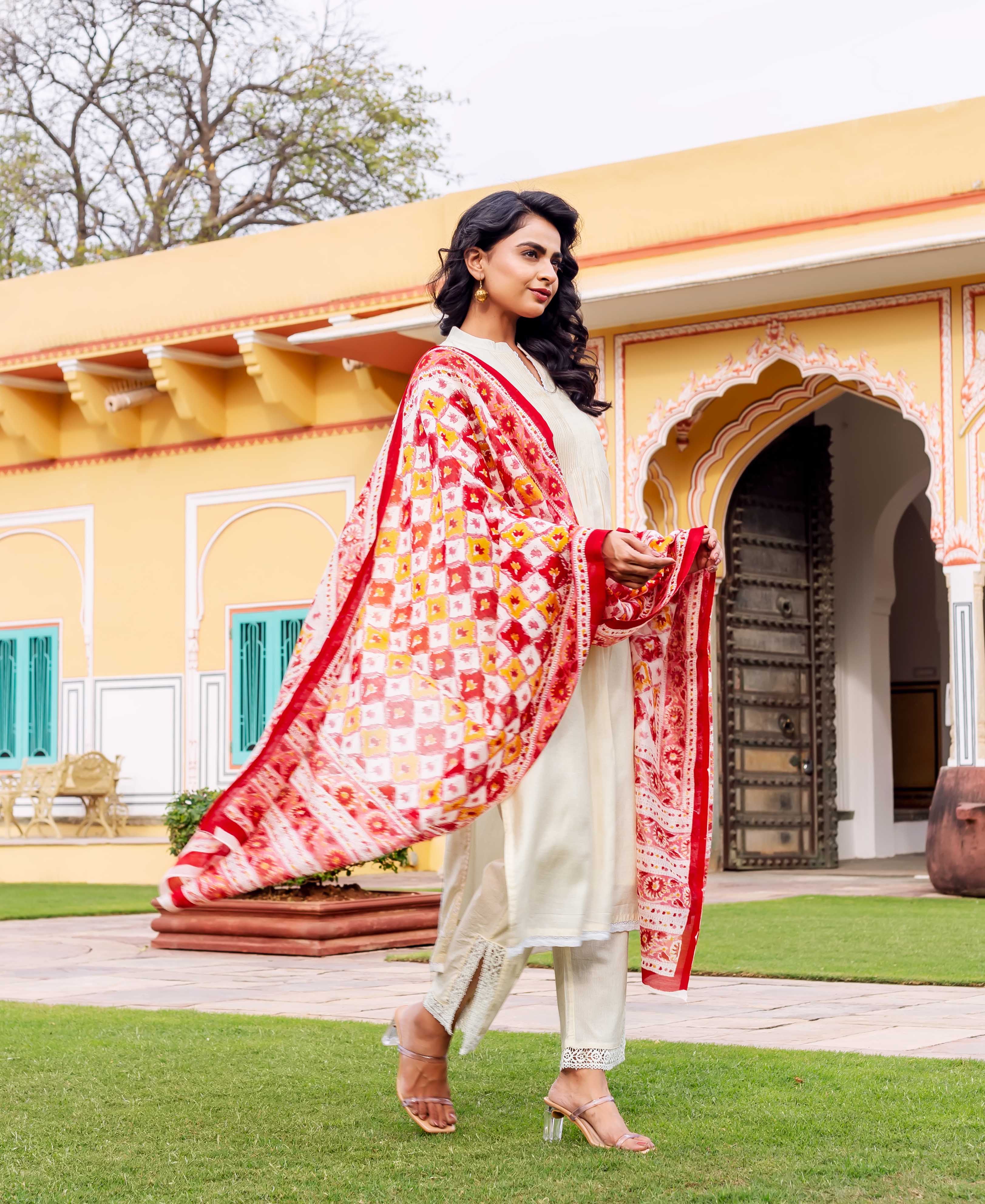 Woman in cream outfit with vibrant red and yellow hand-block-printed shawl outdoors.
