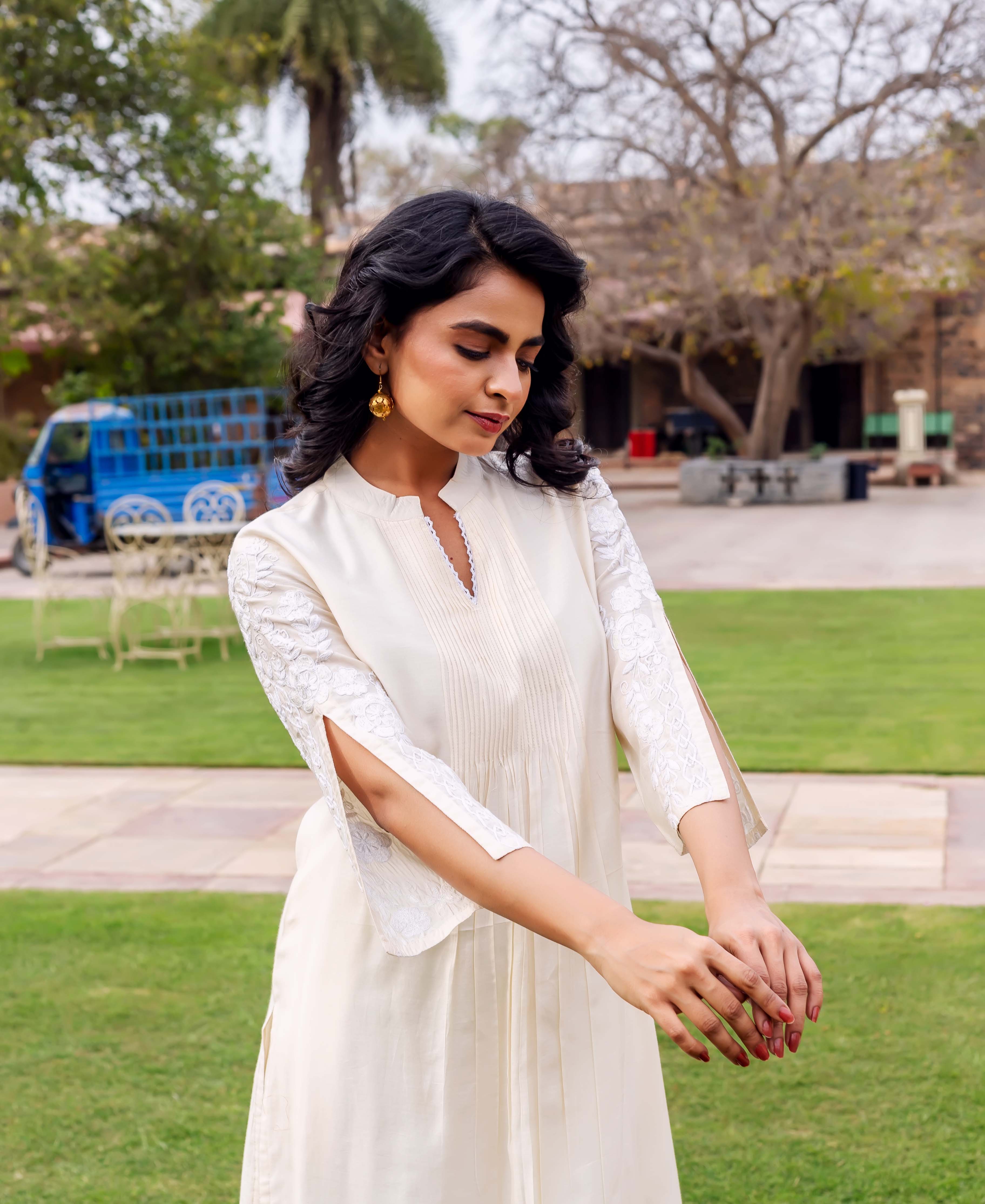 Front view of model wearing an antique white kurta with pintucks and embroidered split sleeves.
