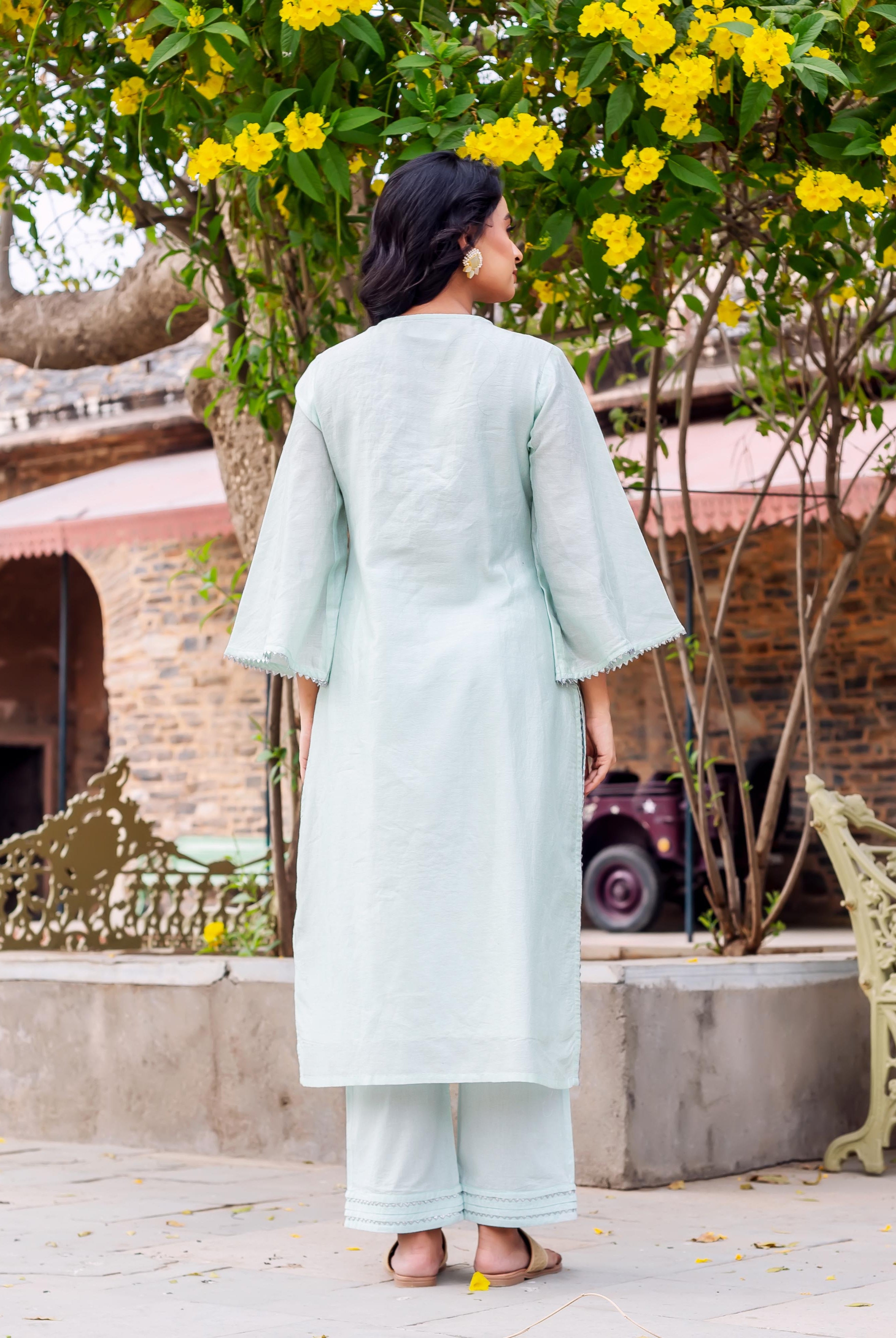 Model from behind wearing a mint Chanderi silk kurta set with scalloped trim and gold earrings.