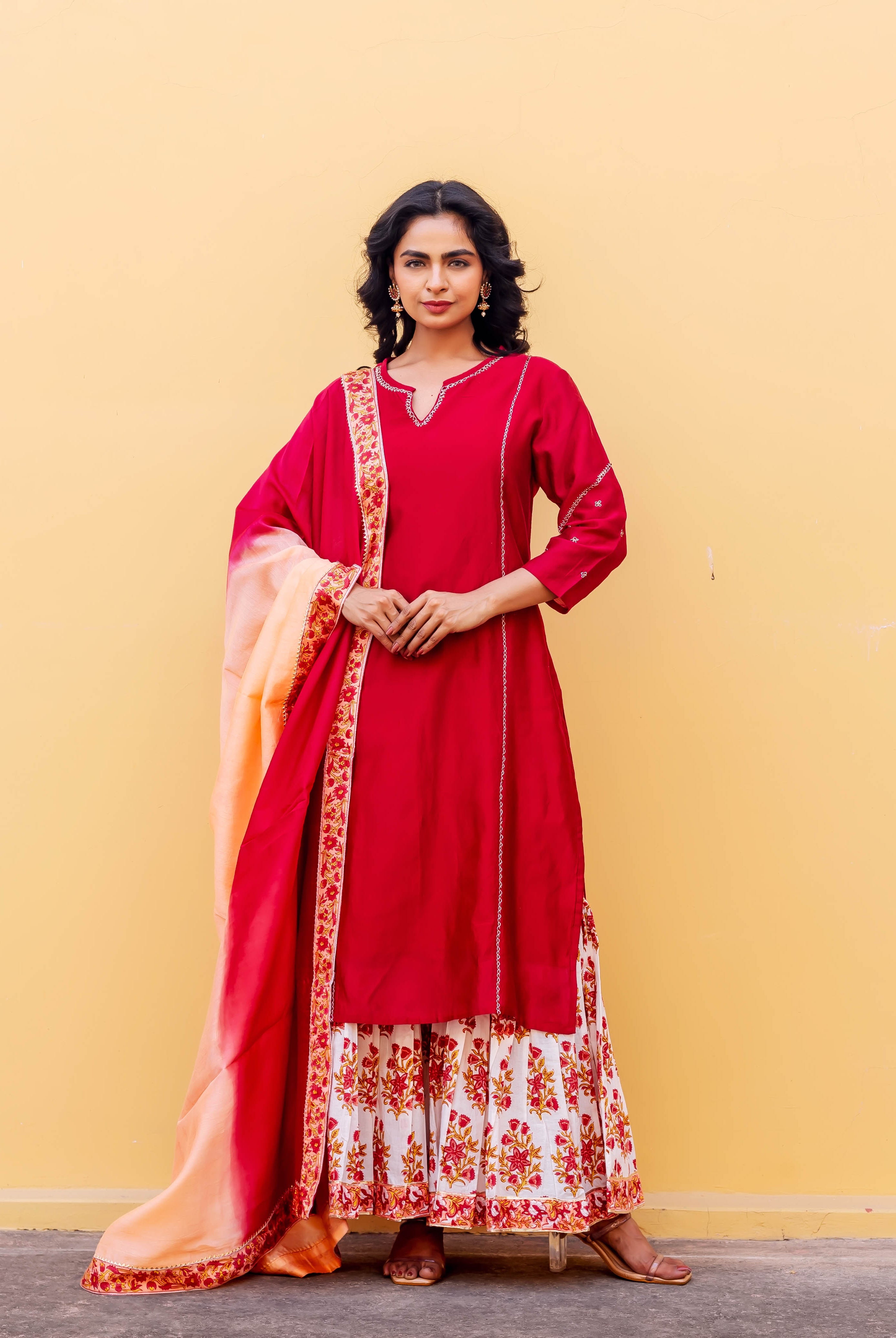 Model in a red embroidered kurta, white hand-block printed sharara, and ombre dupatta.