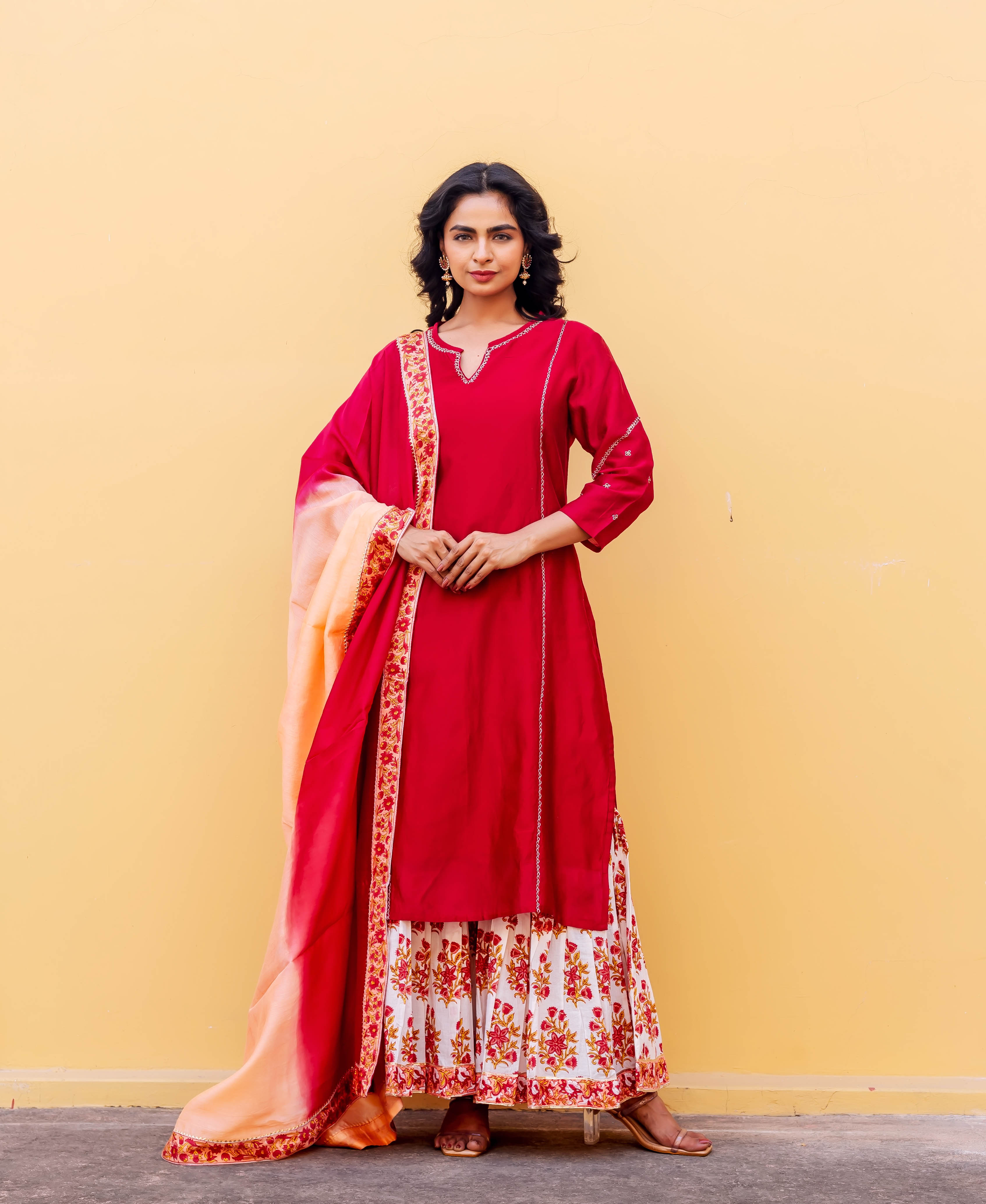 Model in a red embroidered kurta, white hand-block printed sharara, and ombre dupatta.