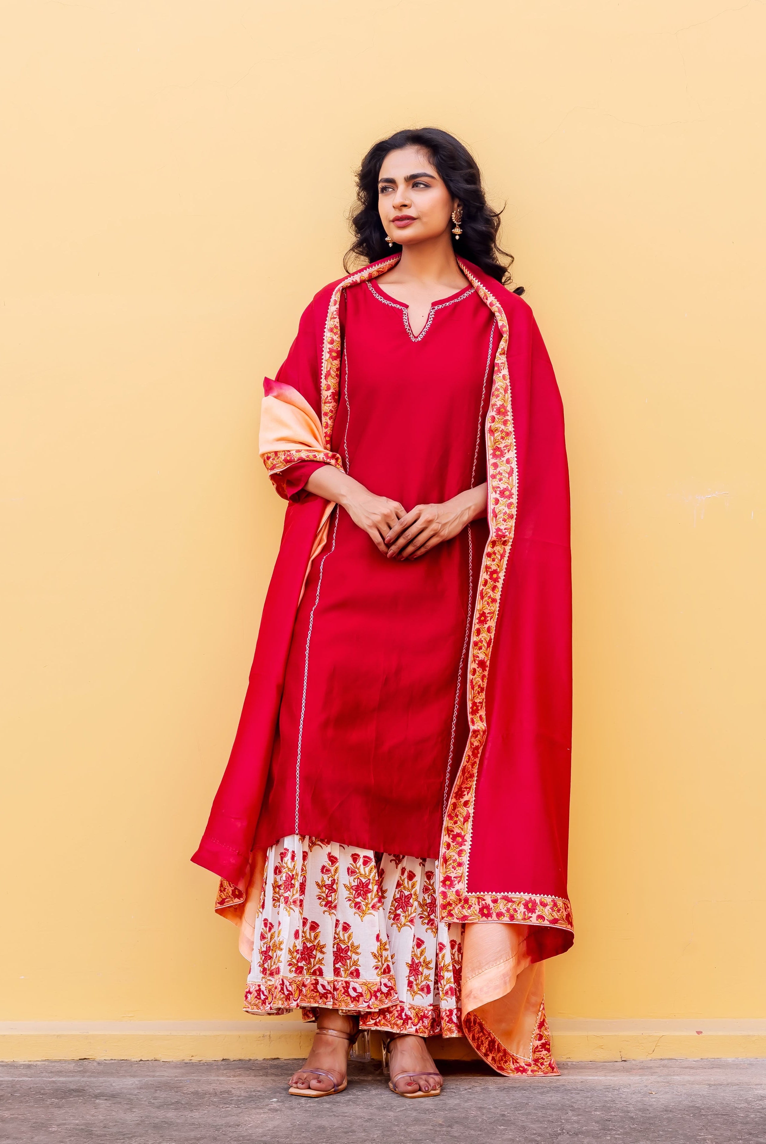 A model wearing a red kurta set with a white and red floral tiered skirt.