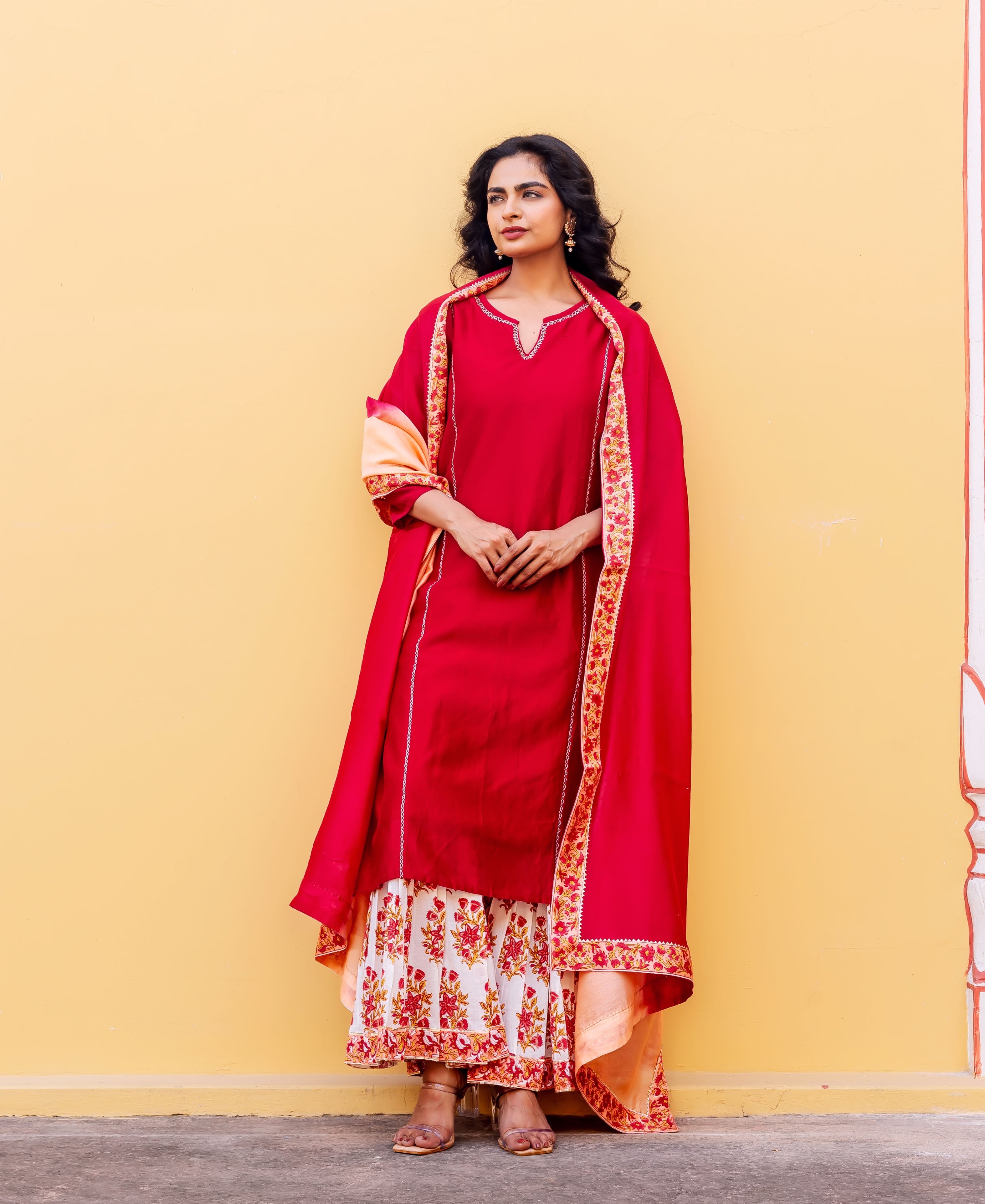 A model wearing a red kurta set with a white and red floral tiered skirt.