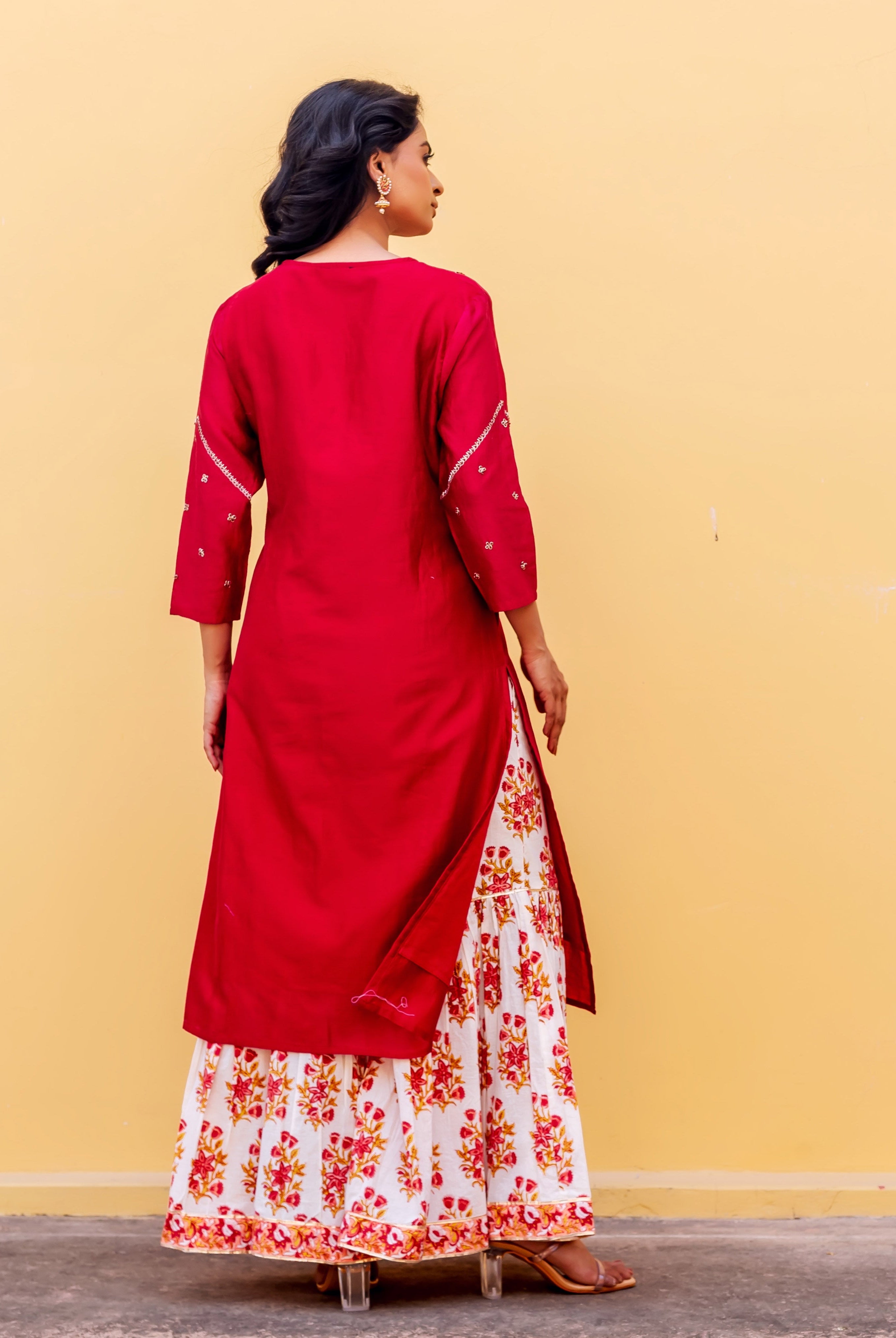 Rear view of model in red kurta with embroidered sleeves and white floral printed skirt.