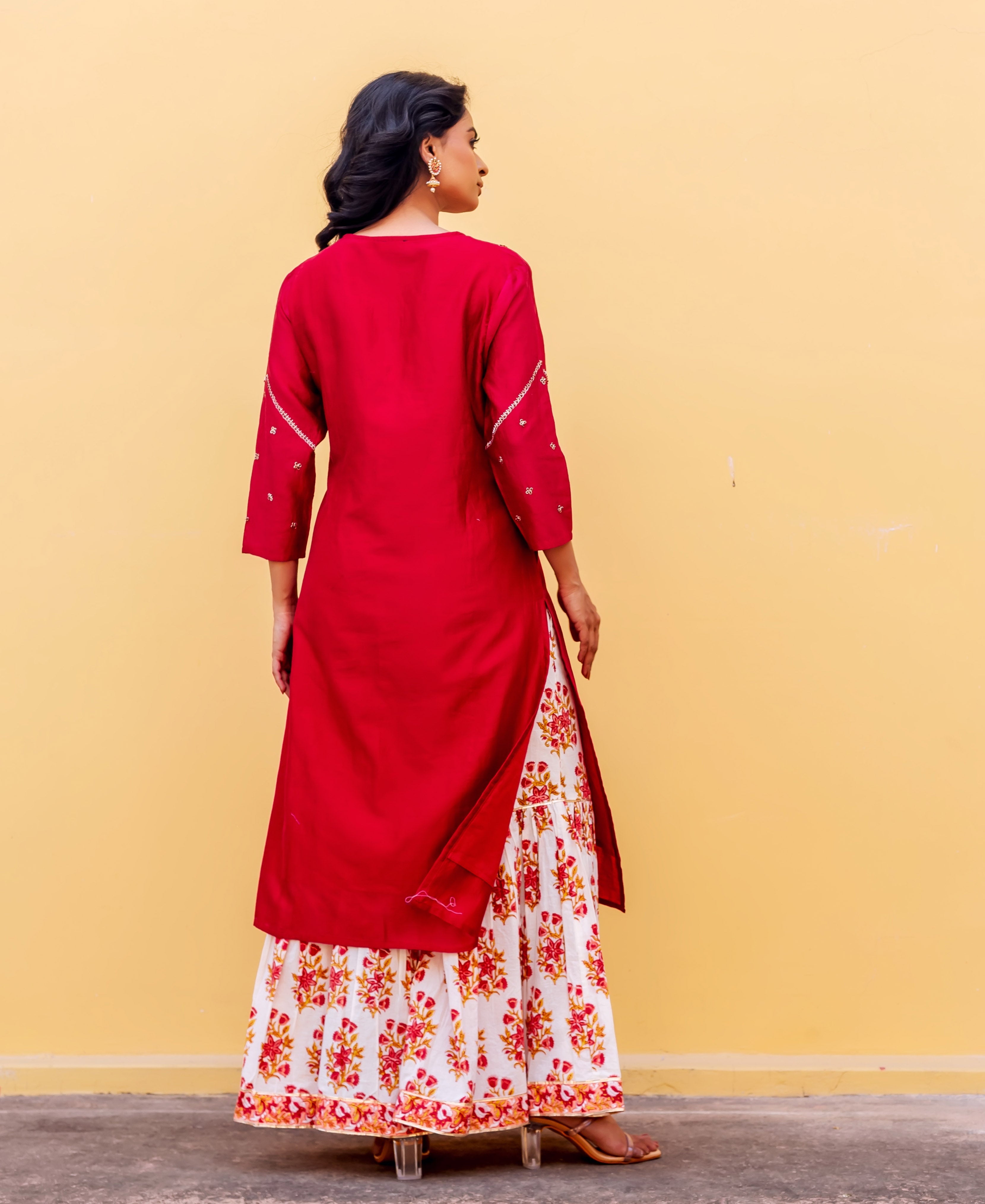 Rear view of model in red kurta with embroidered sleeves and white floral printed skirt.