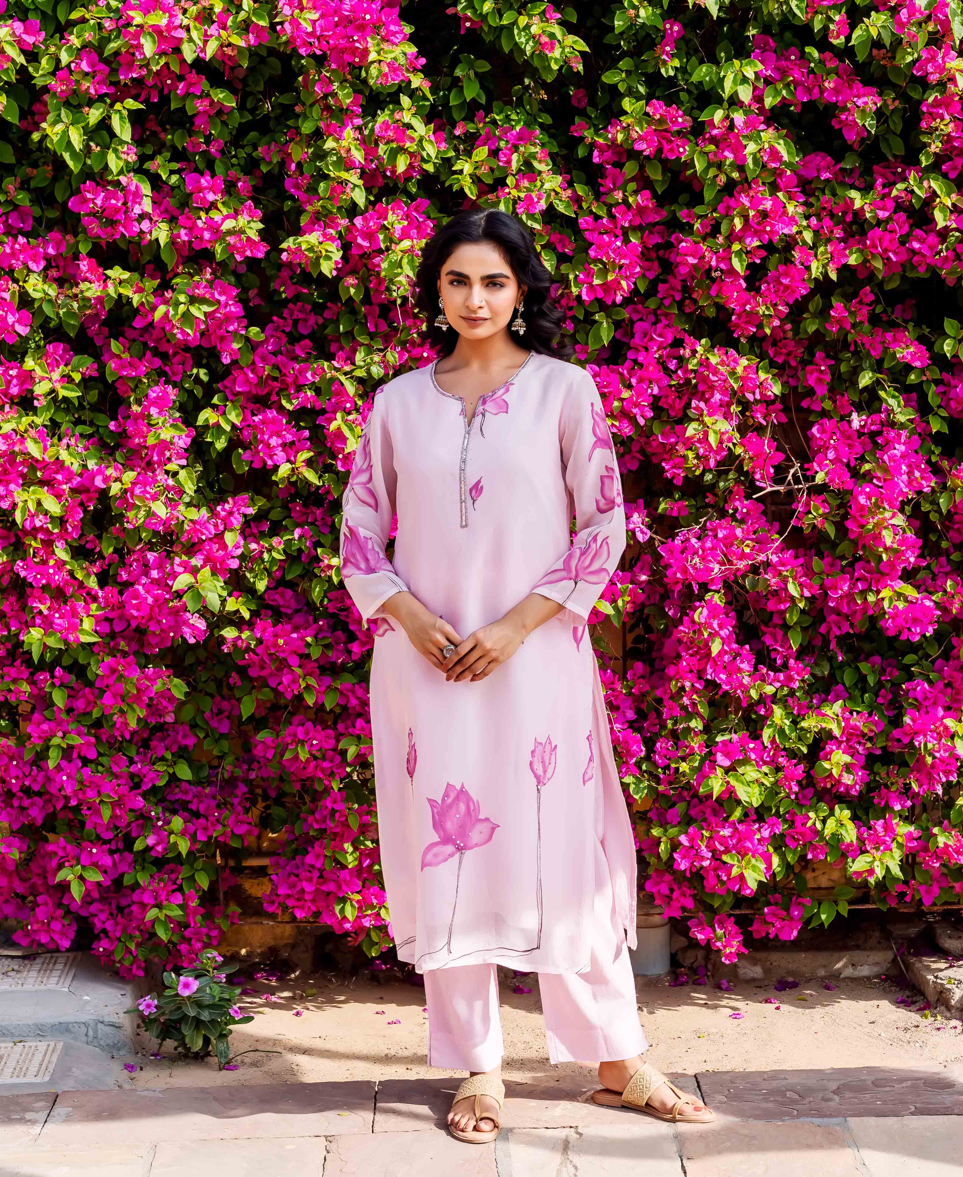 Model wears pink hand-block-printed organza kurta and trousers with lotus floral design.
