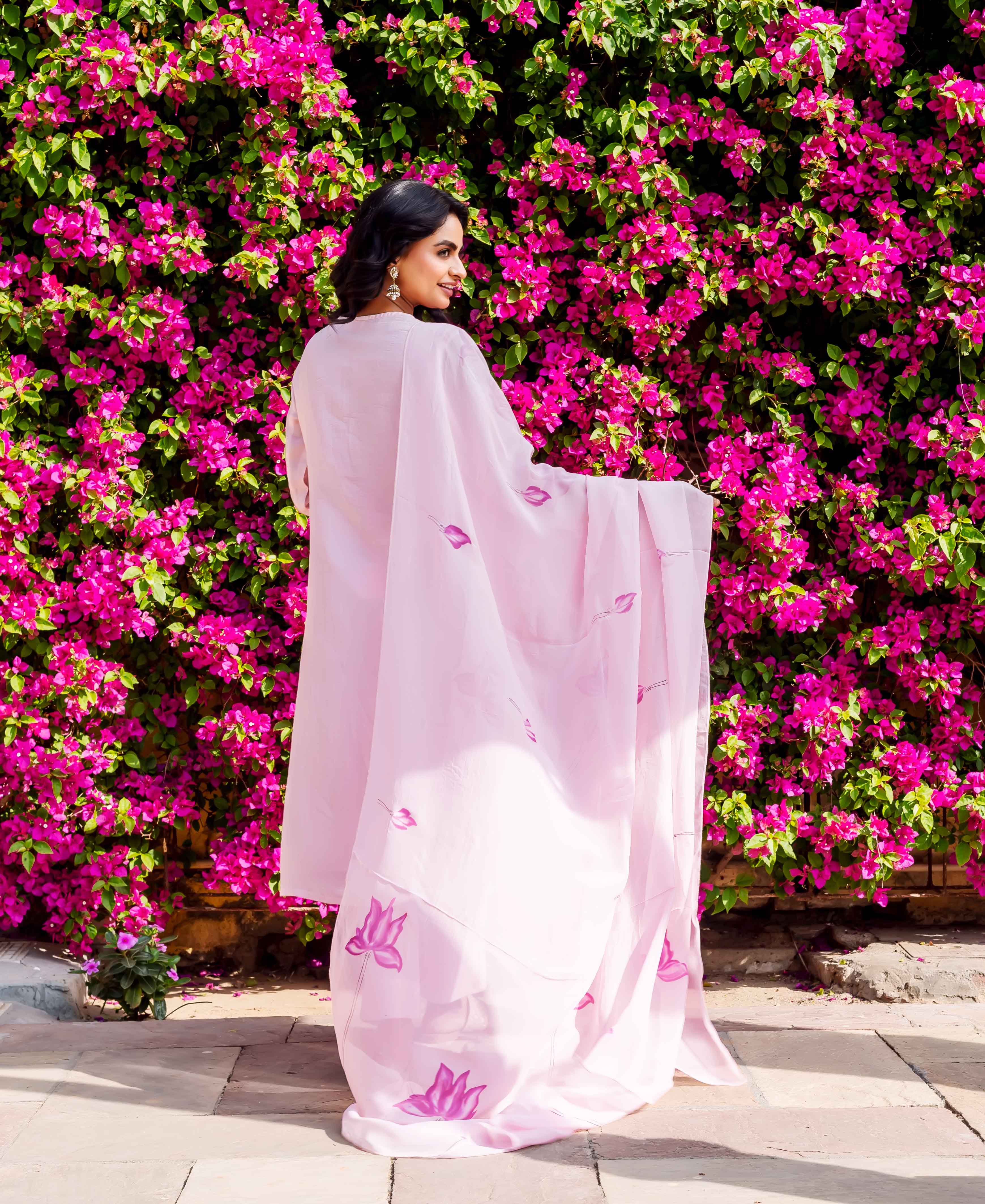 Woman in flowing pink organza kurta with hand-block-printed purple lotus motifs, standing outdoors.