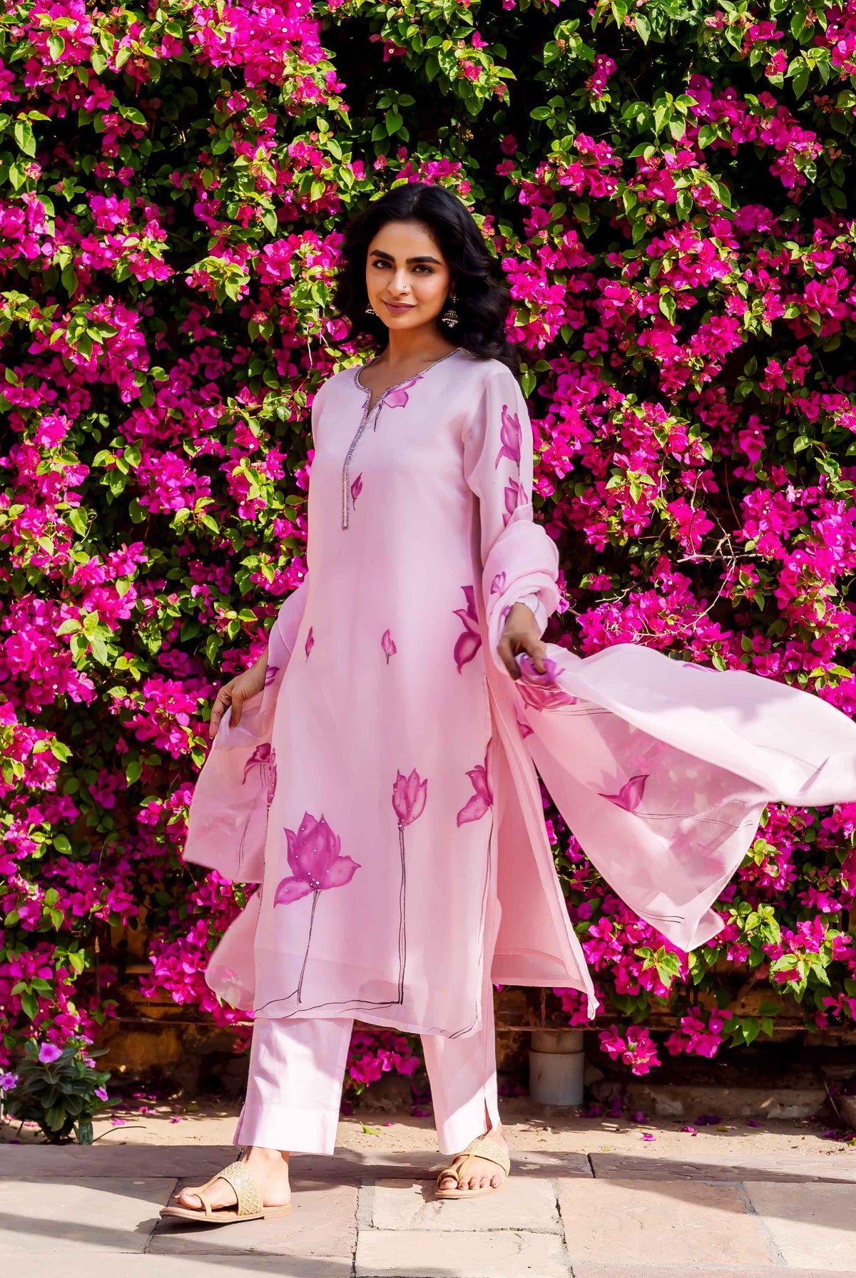 Model wears full pink organza kurta set with hand-block-printed pink lotus designs.