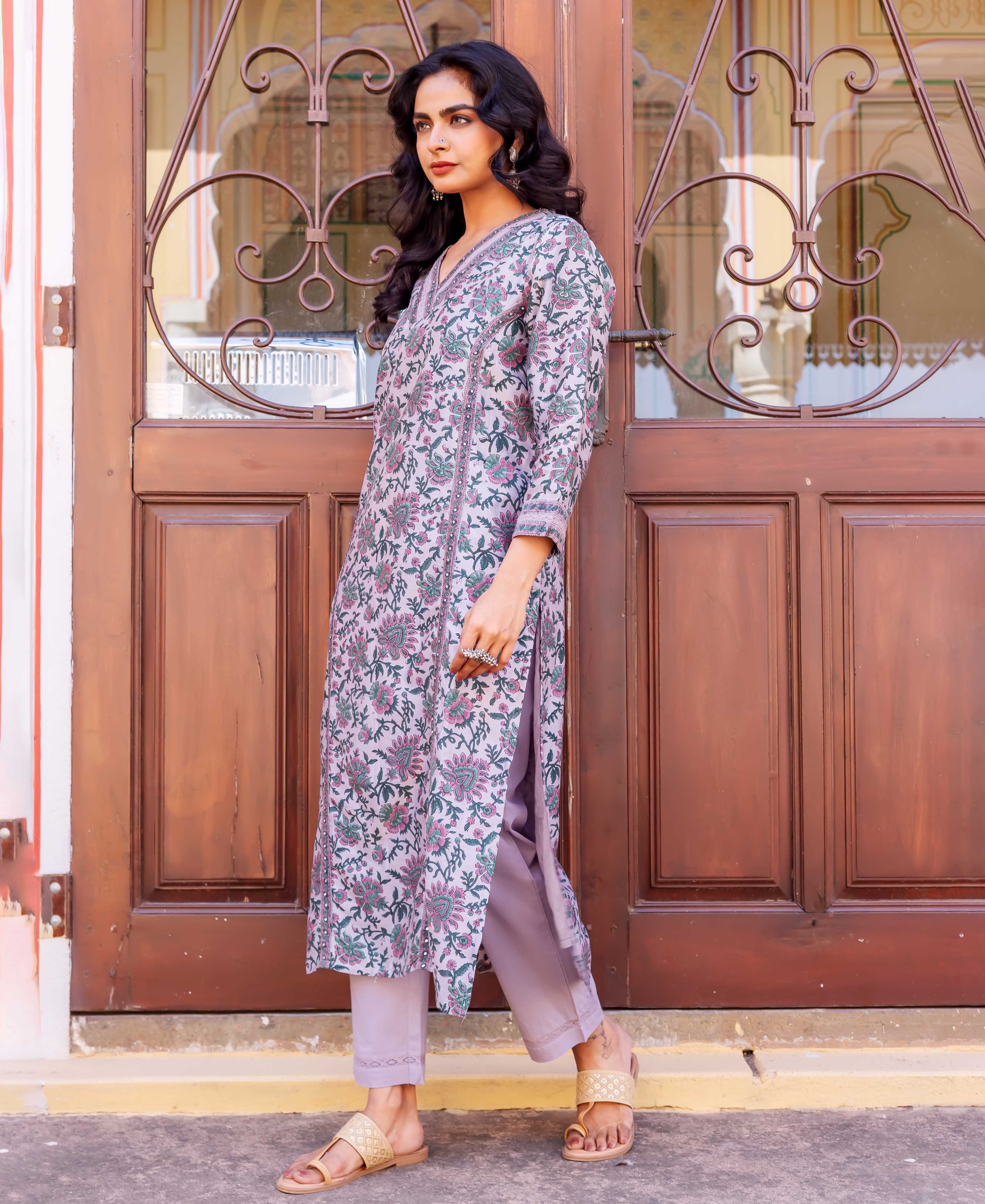 Woman wearing lilac kurta with pink floral print and green leaves, paired with light purple pants.