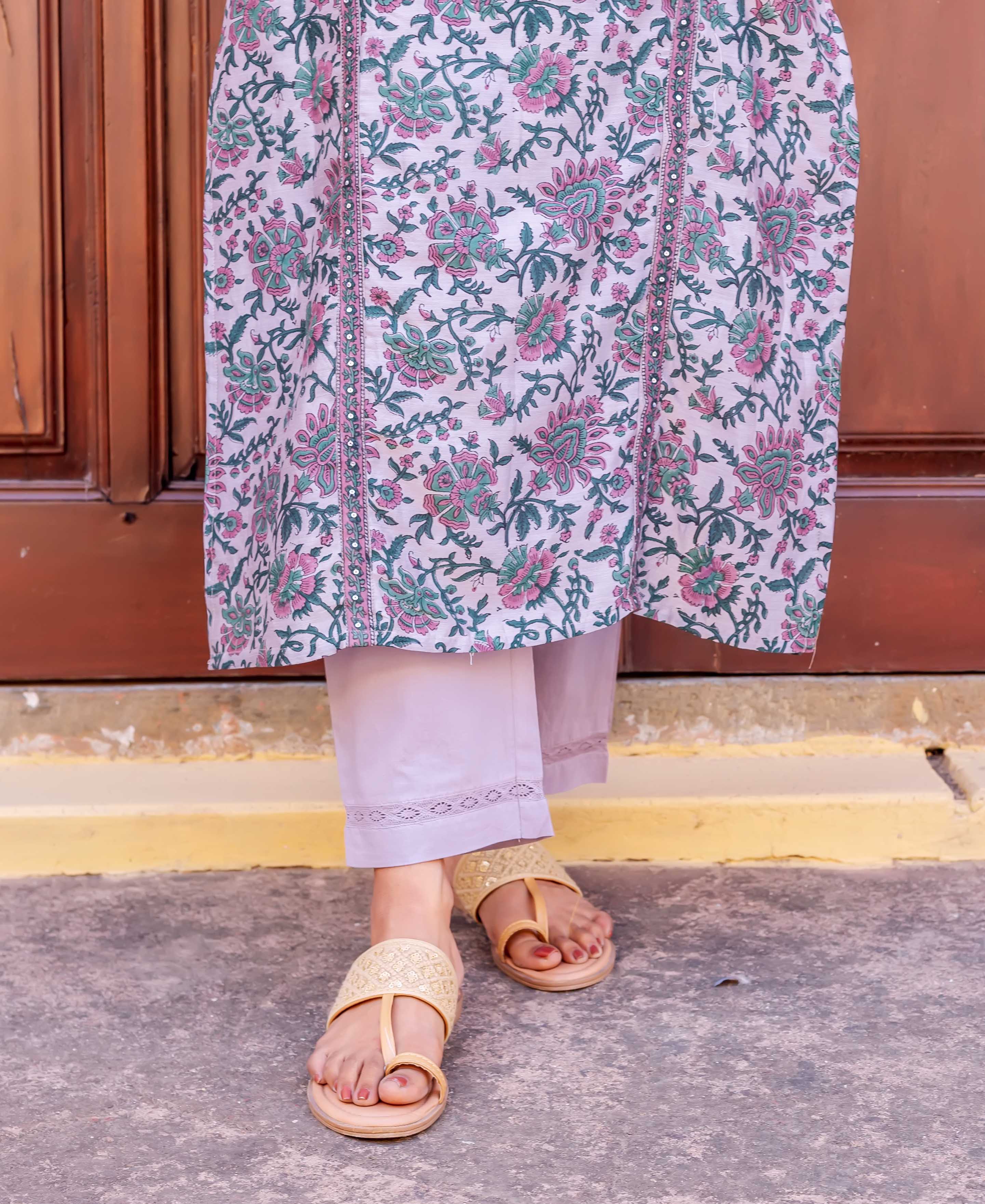 Low angle of model wearing floral block-printed white kurta, lilac pants, and tan sandals.