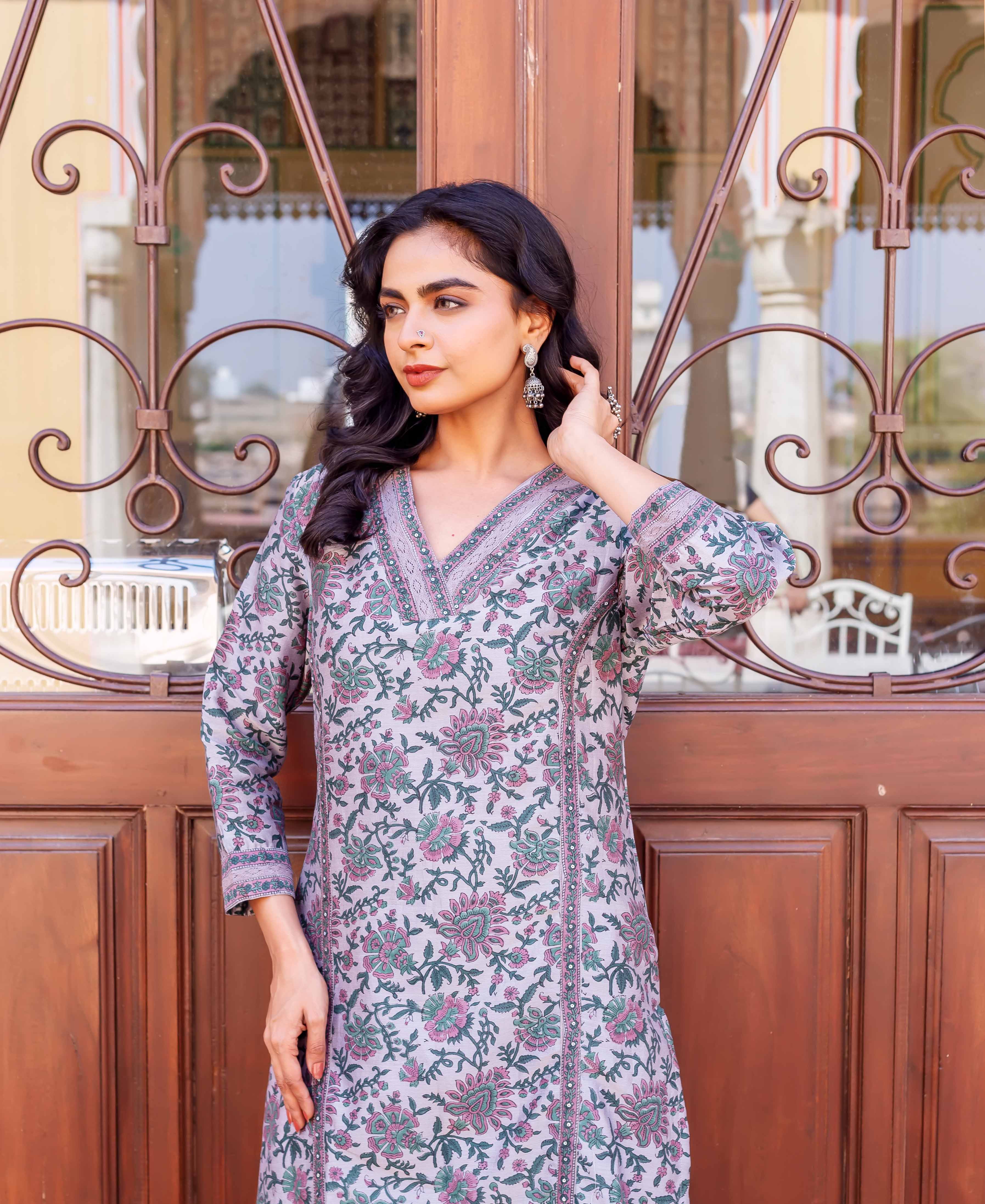 Woman wearing lilac kurta with pink and green floral hand-block-printed design, standing by gate.