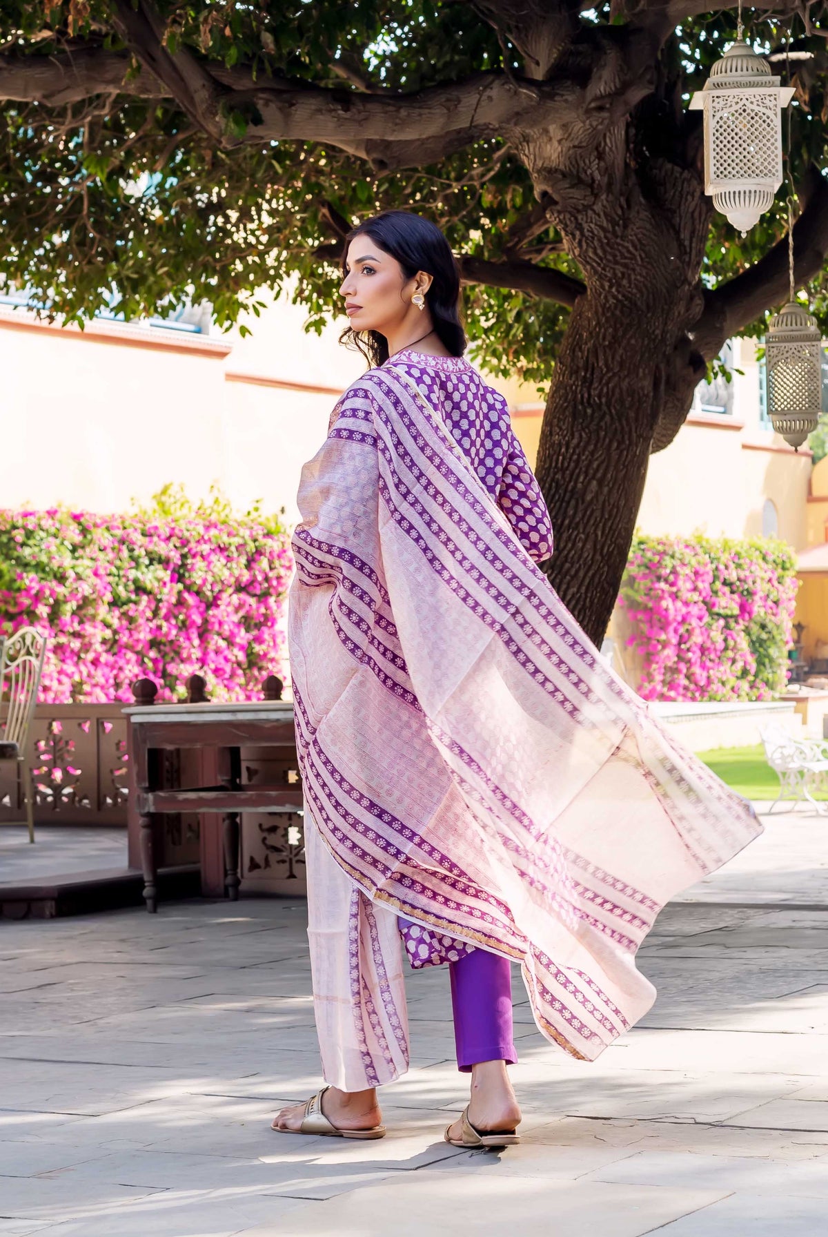 Back view of model in purple polka-dot kurta, flowing pink and purple block print dupatta, purple pants.