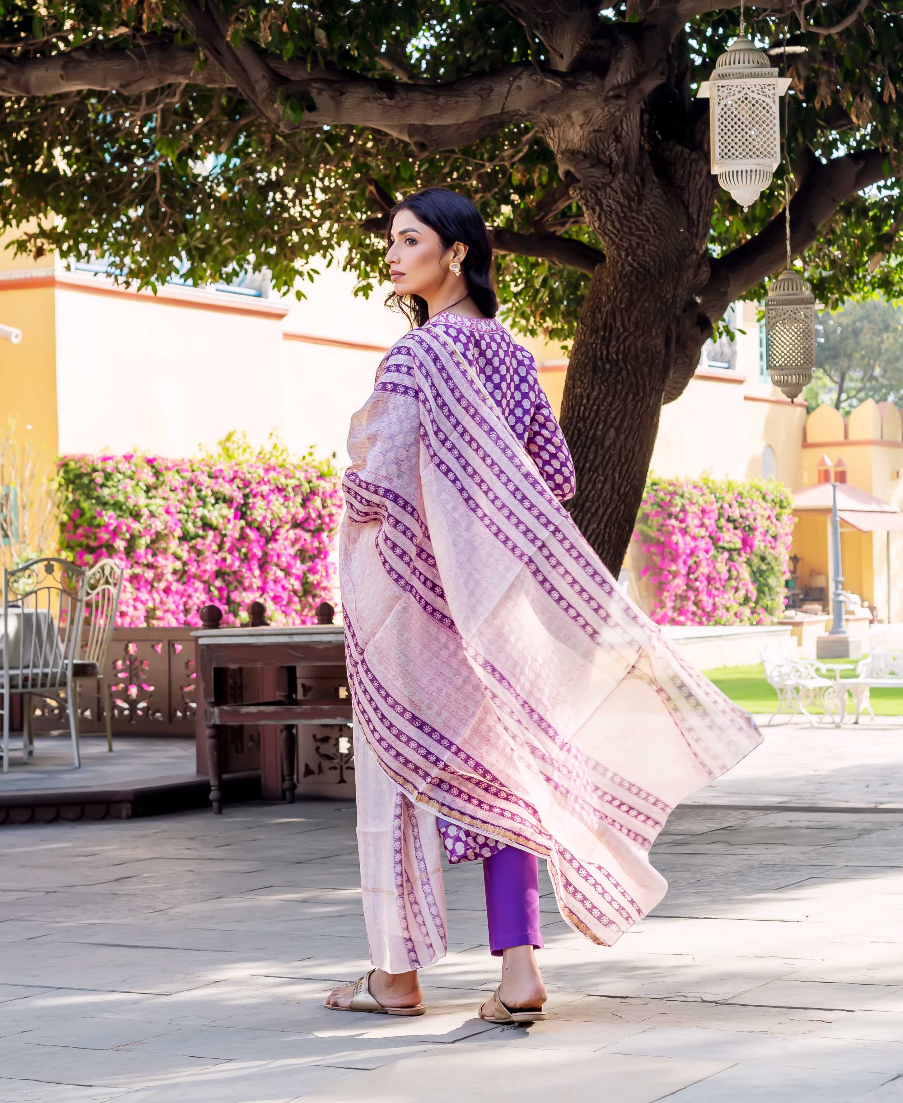 Back view of model in purple polka-dot kurta, flowing pink and purple block print dupatta, purple pants.