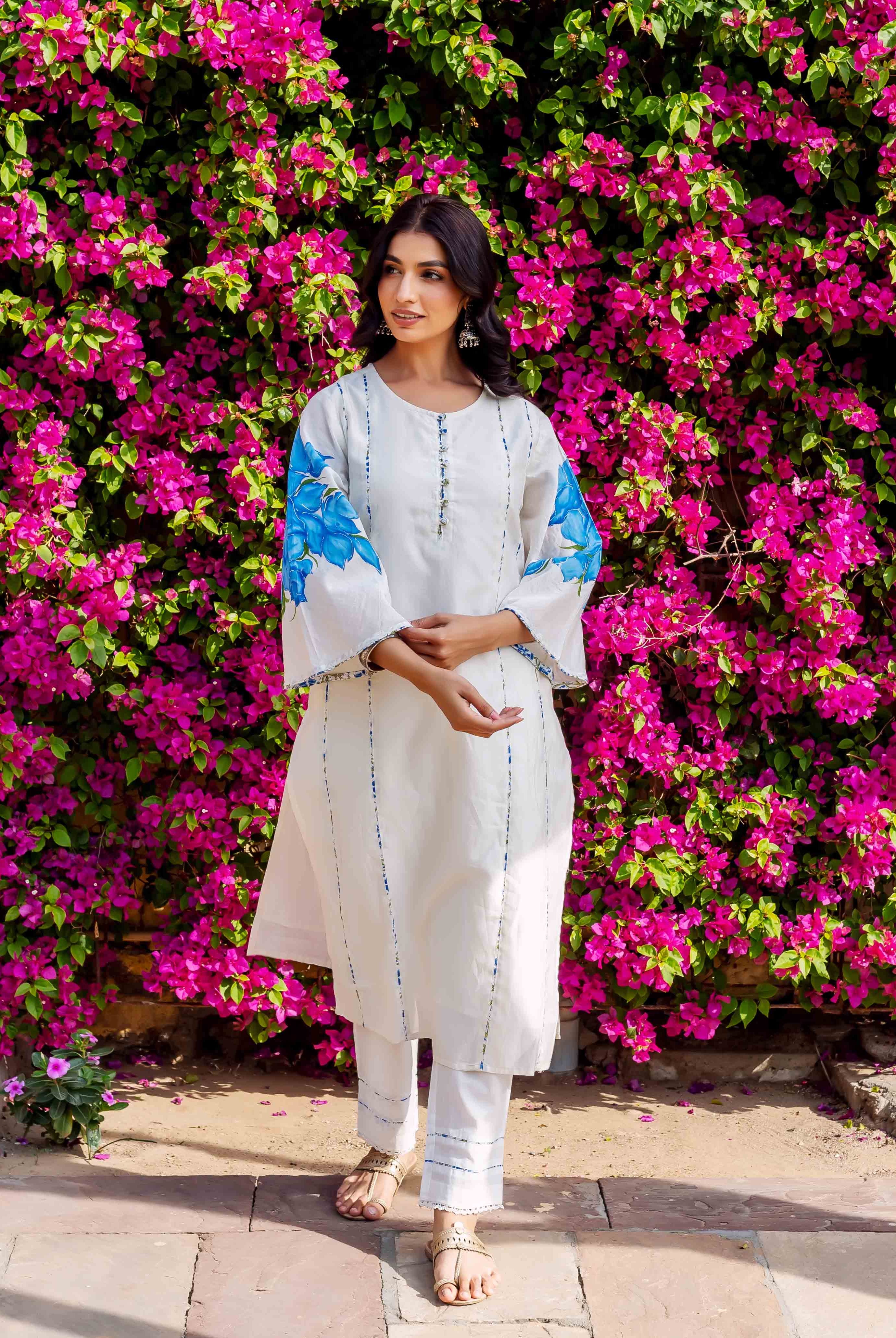 Full-length model wearing white kurta set with blue brush-painted floral sleeves and stripes.