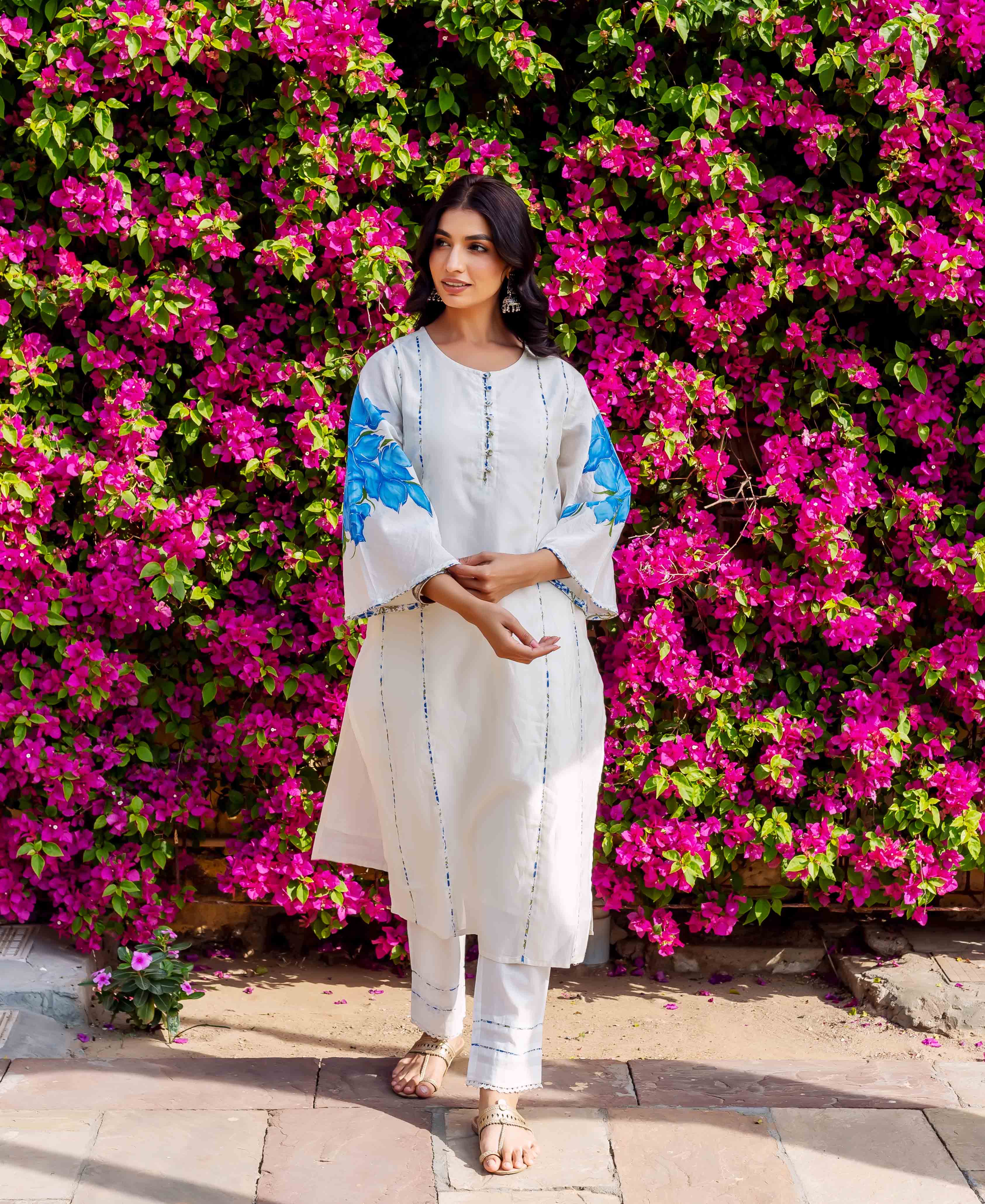 Full-length model wearing white kurta set with blue brush-painted floral sleeves and stripes.
