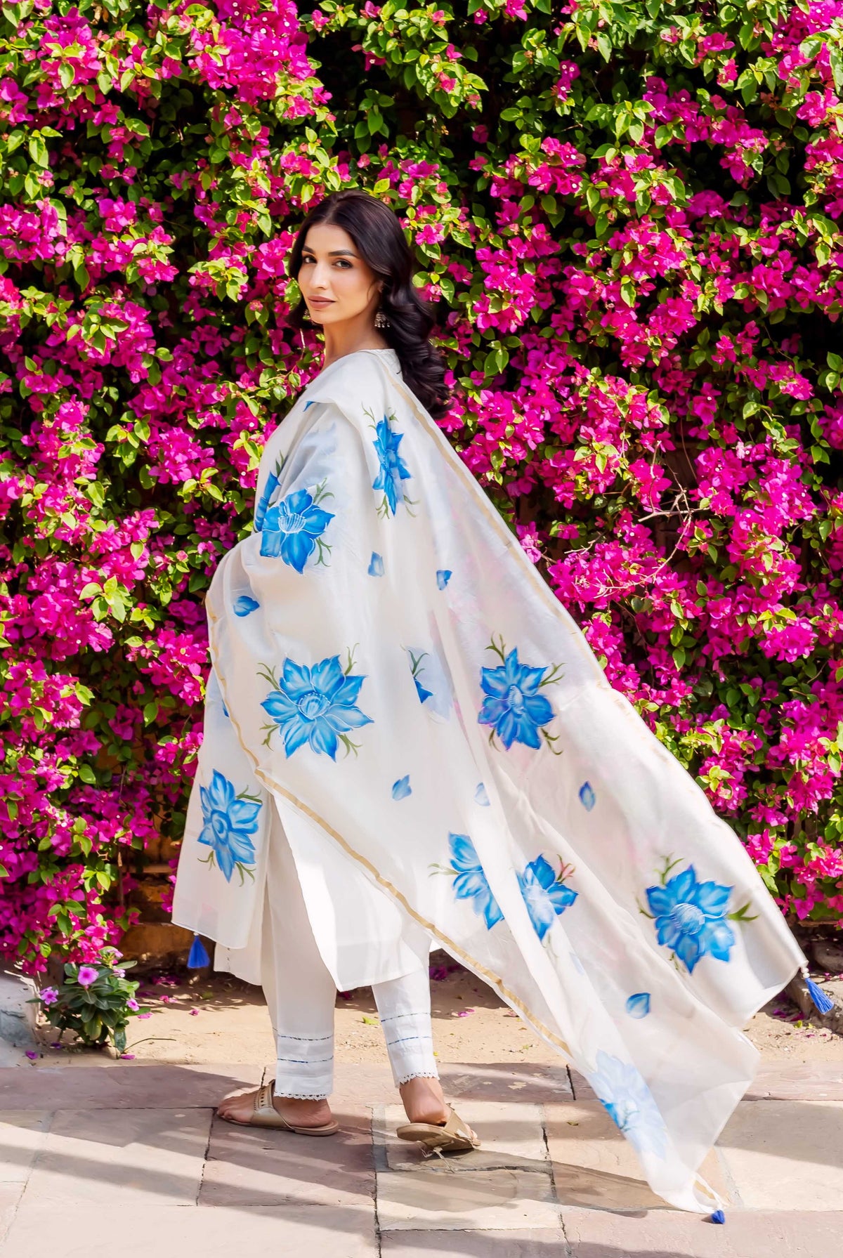 Model wears white ethnic set, flowing dupatta with blue brush-painted florals.
