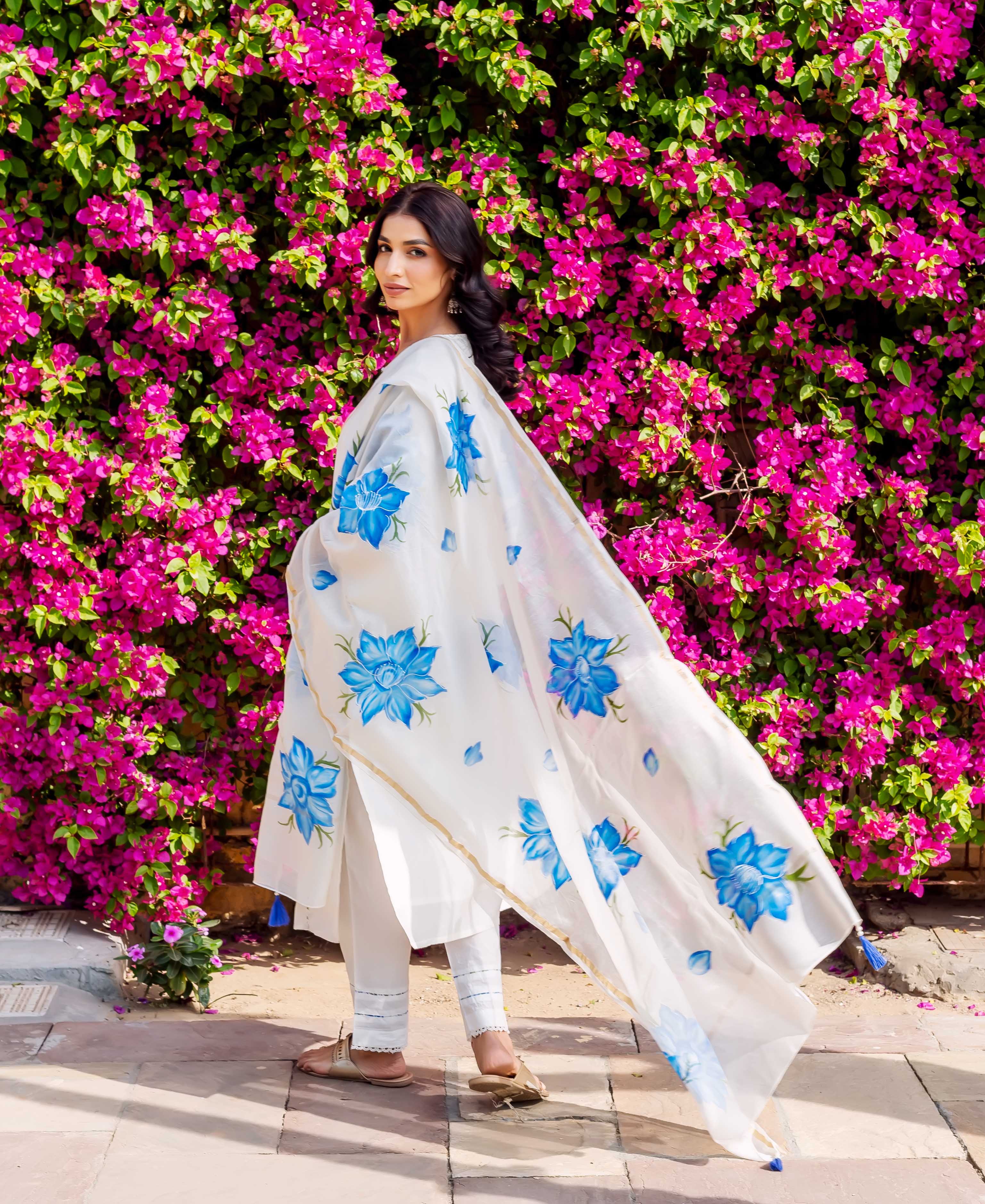Model wears white ethnic set, flowing dupatta with blue brush-painted florals.