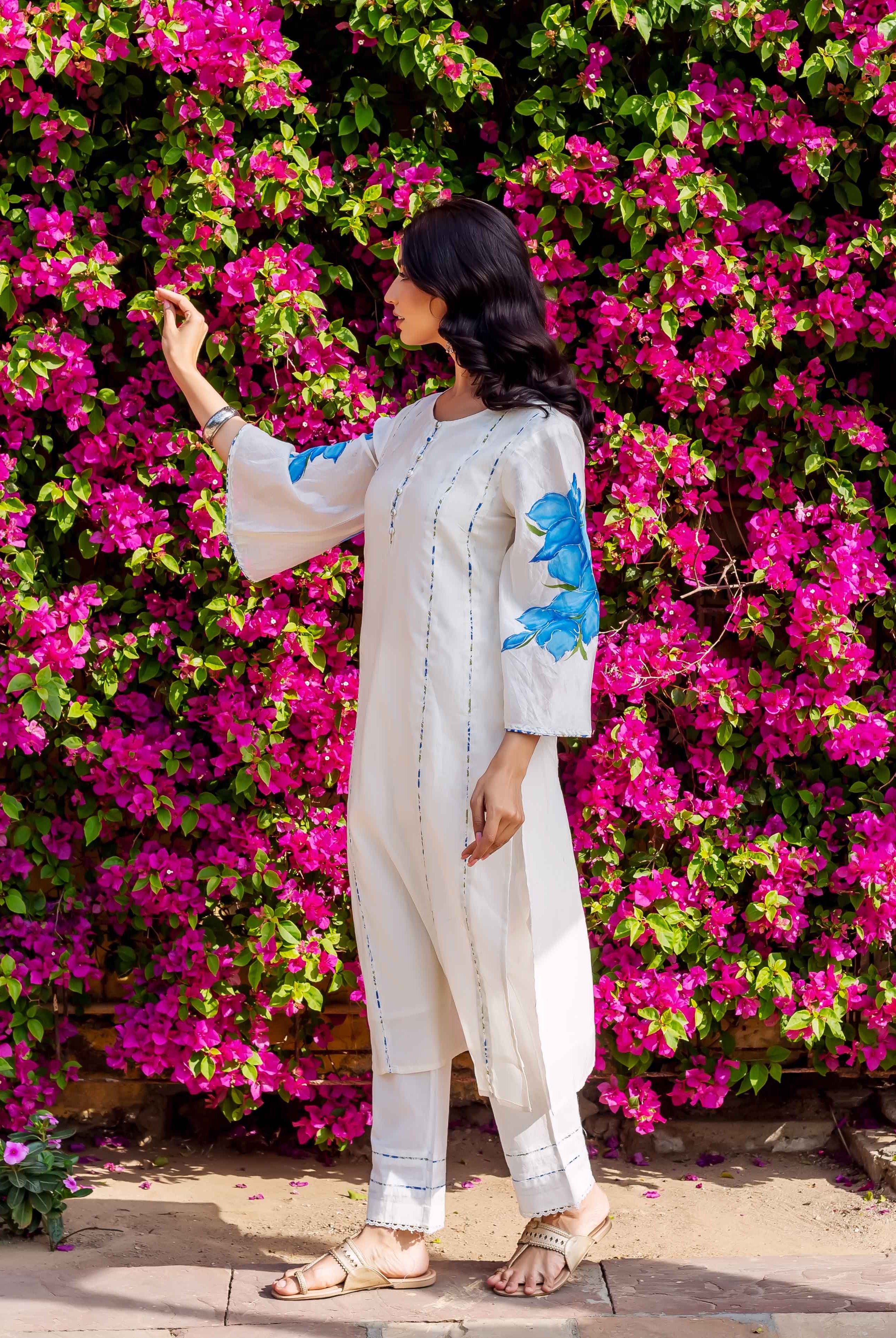 Side angle of model wearing cream kurta and pants with blue brush-painted floral sleeves.
